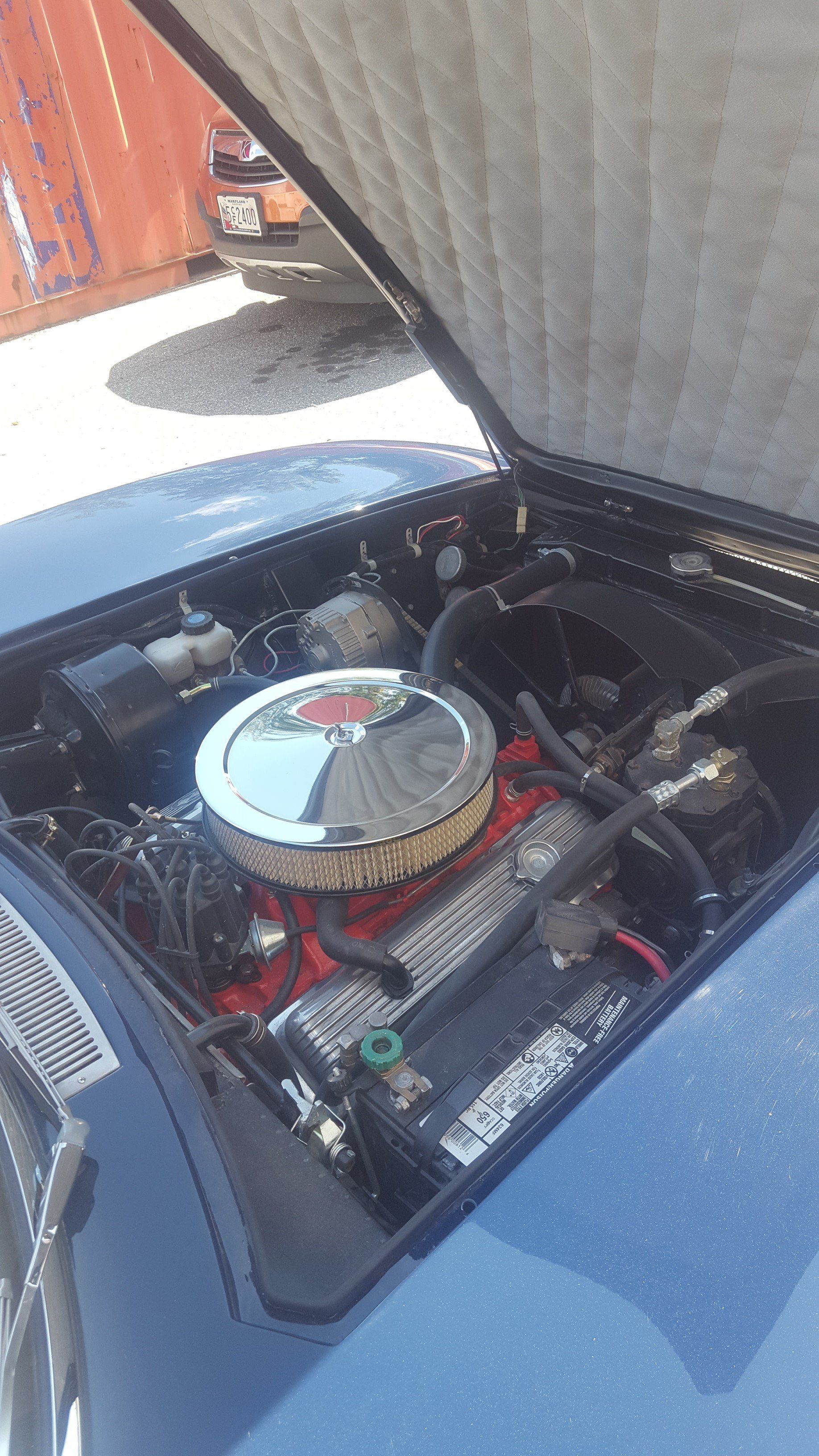 Blue classic car engine bay with chrome air filter, open hood.
