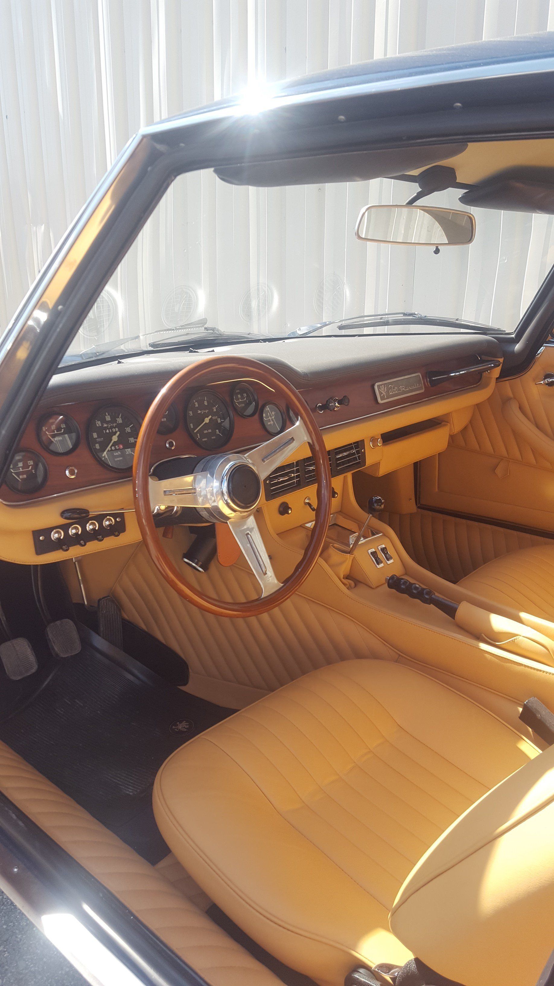 Interior of a vintage car with tan leather seats and a wooden steering wheel, dashboard, and details.