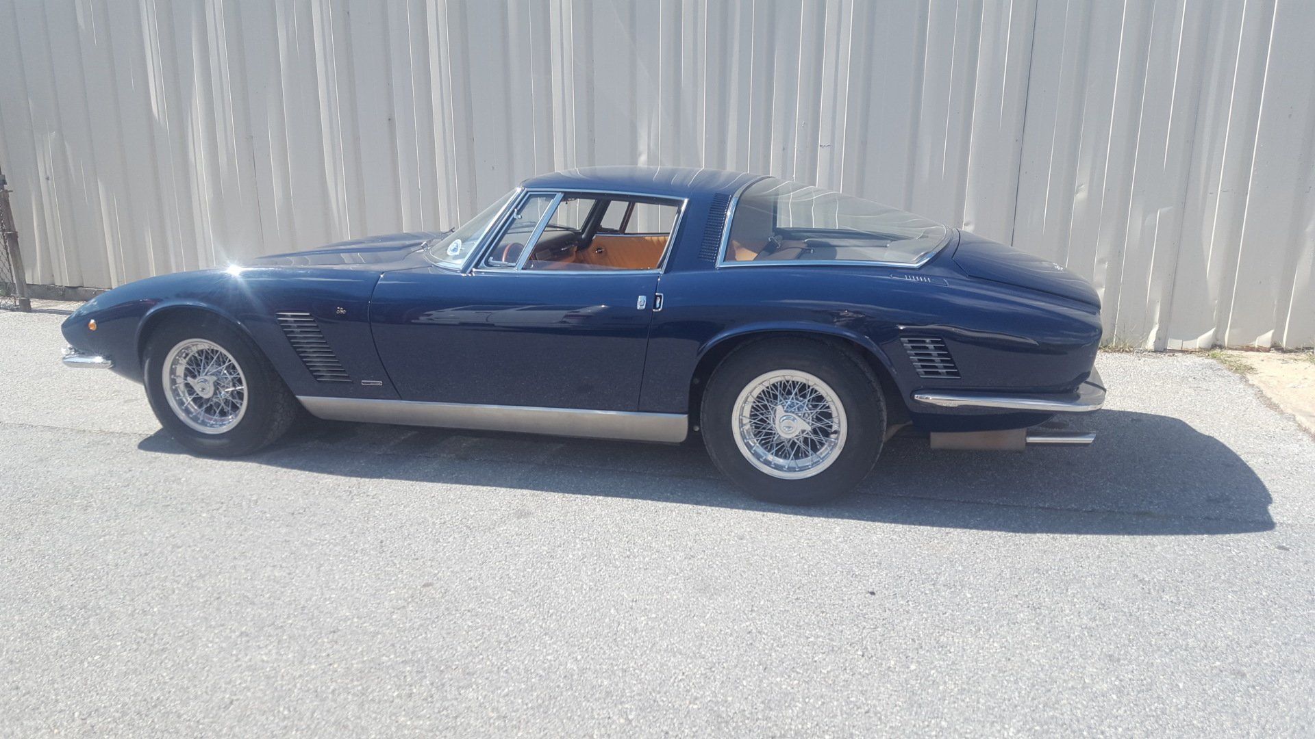 Blue Jensen Interceptor coupe parked on asphalt, bright sunlight.