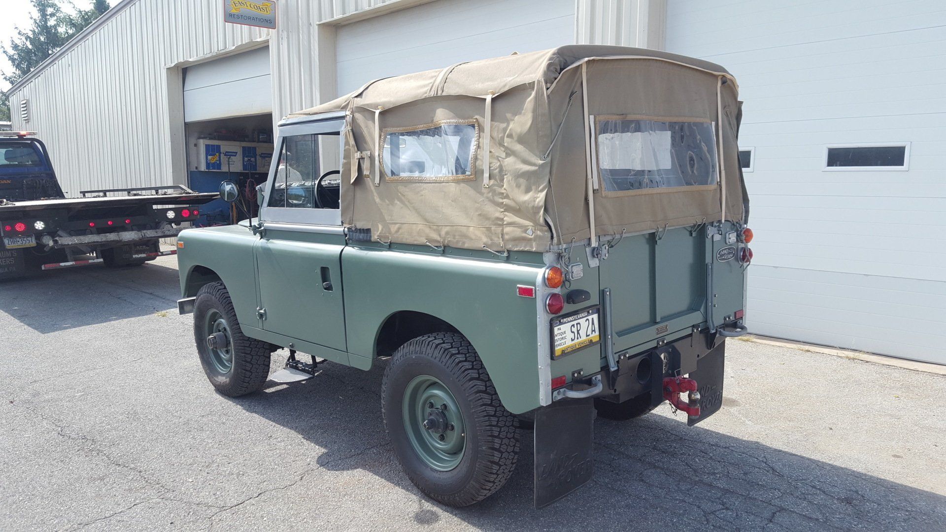 Green Land Rover with canvas top parked in front of garage.