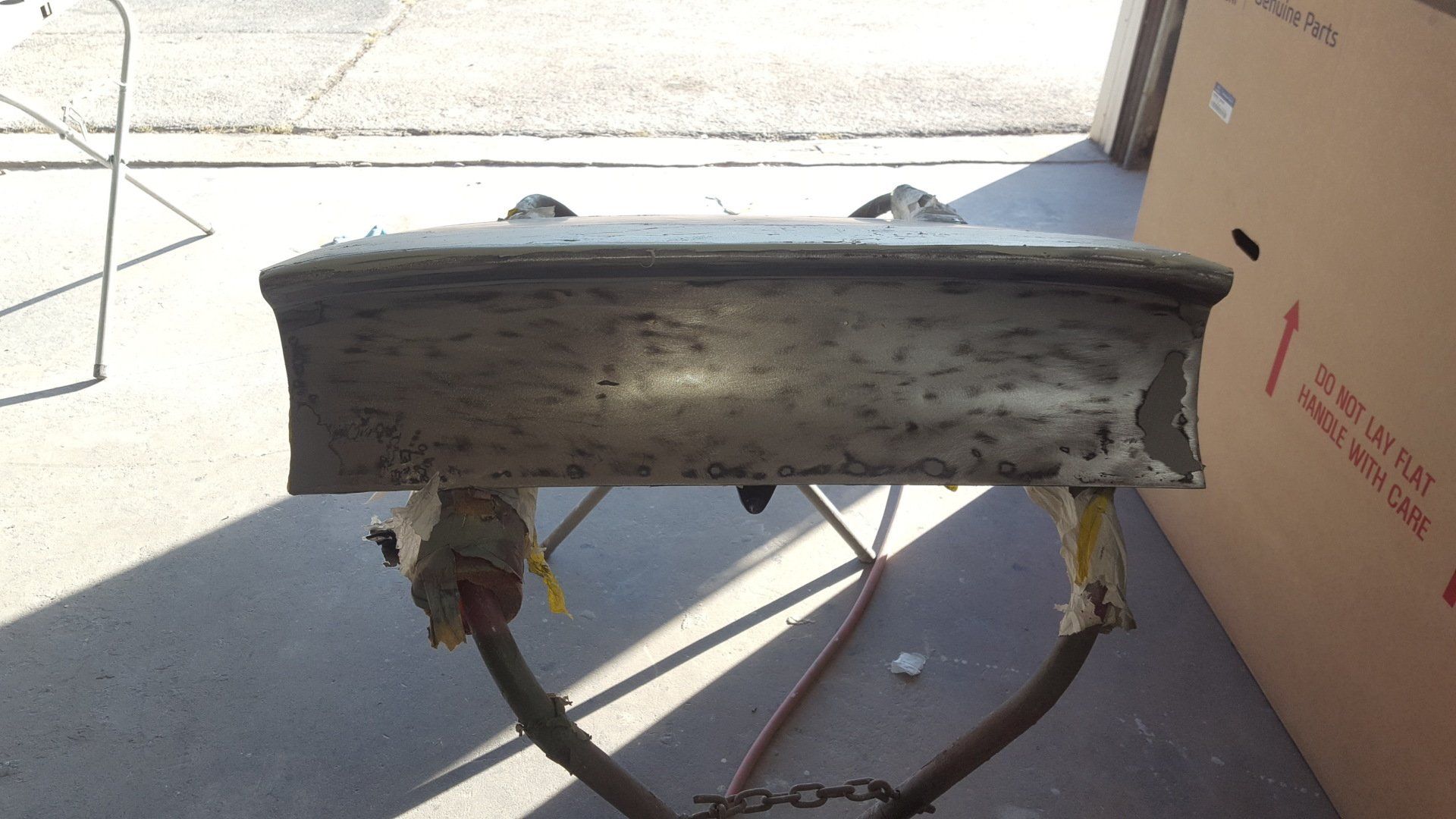 Metal car hood, primed and mounted on a stand, outdoors. Preparing for paint.