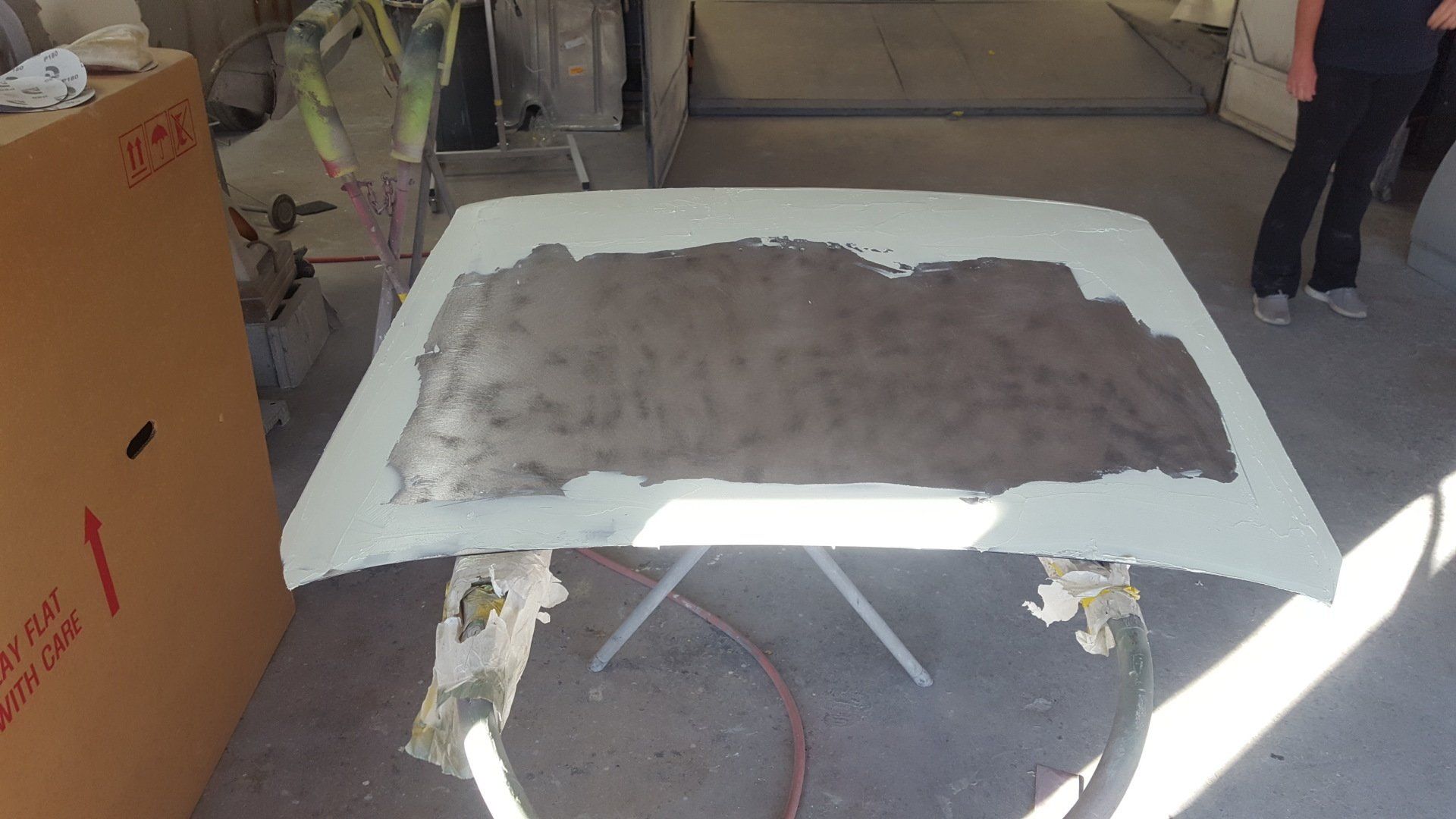 Car hood on a stand, primed and partially sanded in a garage.