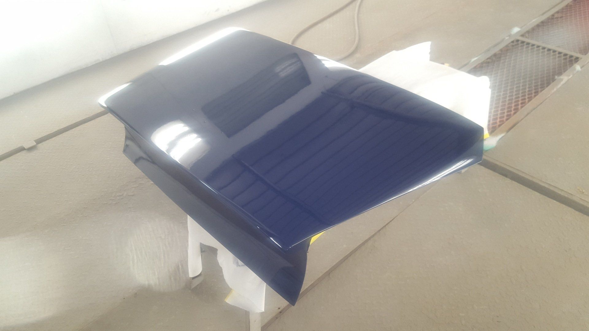 Blue car hood, freshly painted, resting in a repair shop.