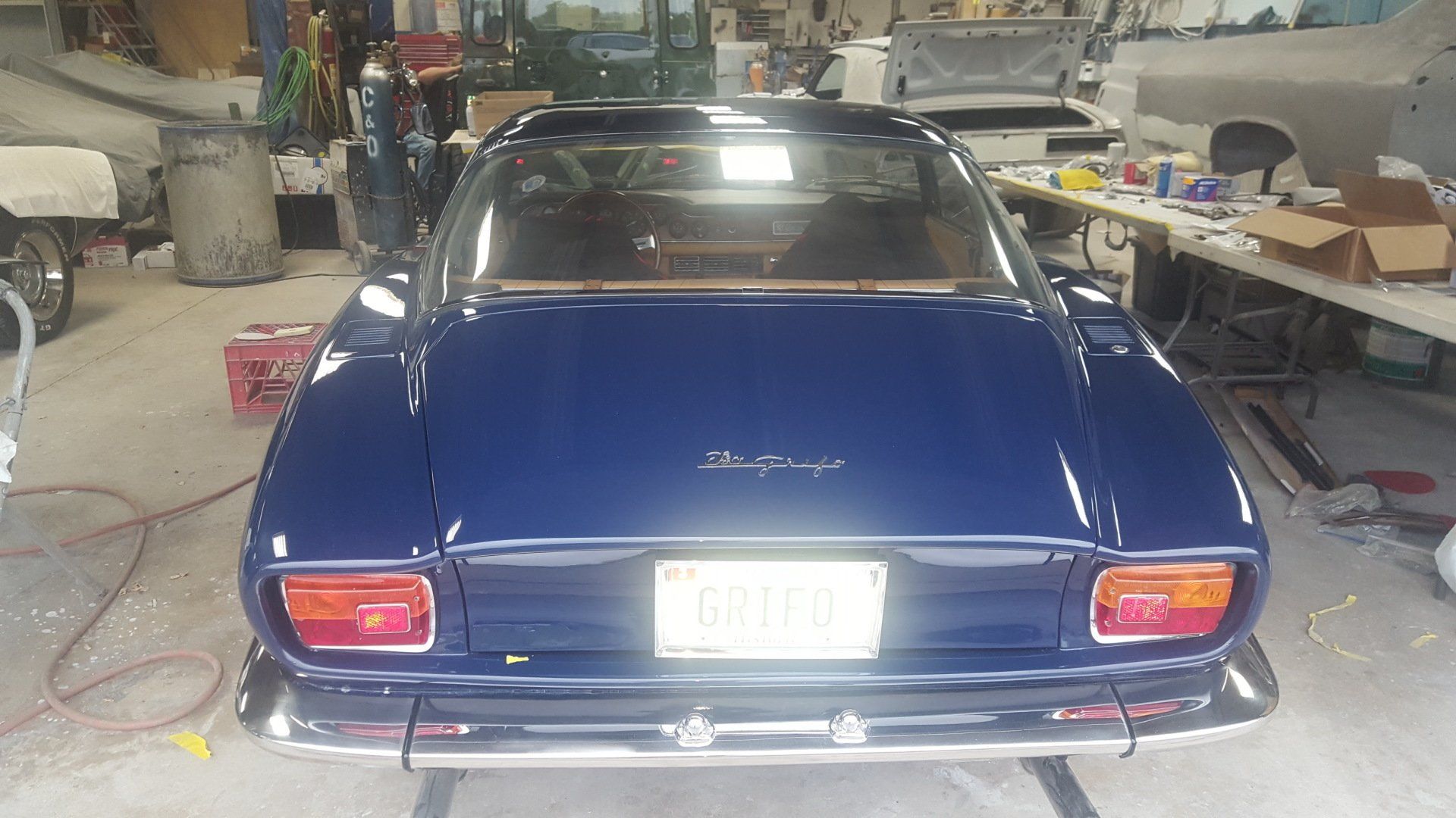 Rear view of a blue vintage car in a garage with a license plate.