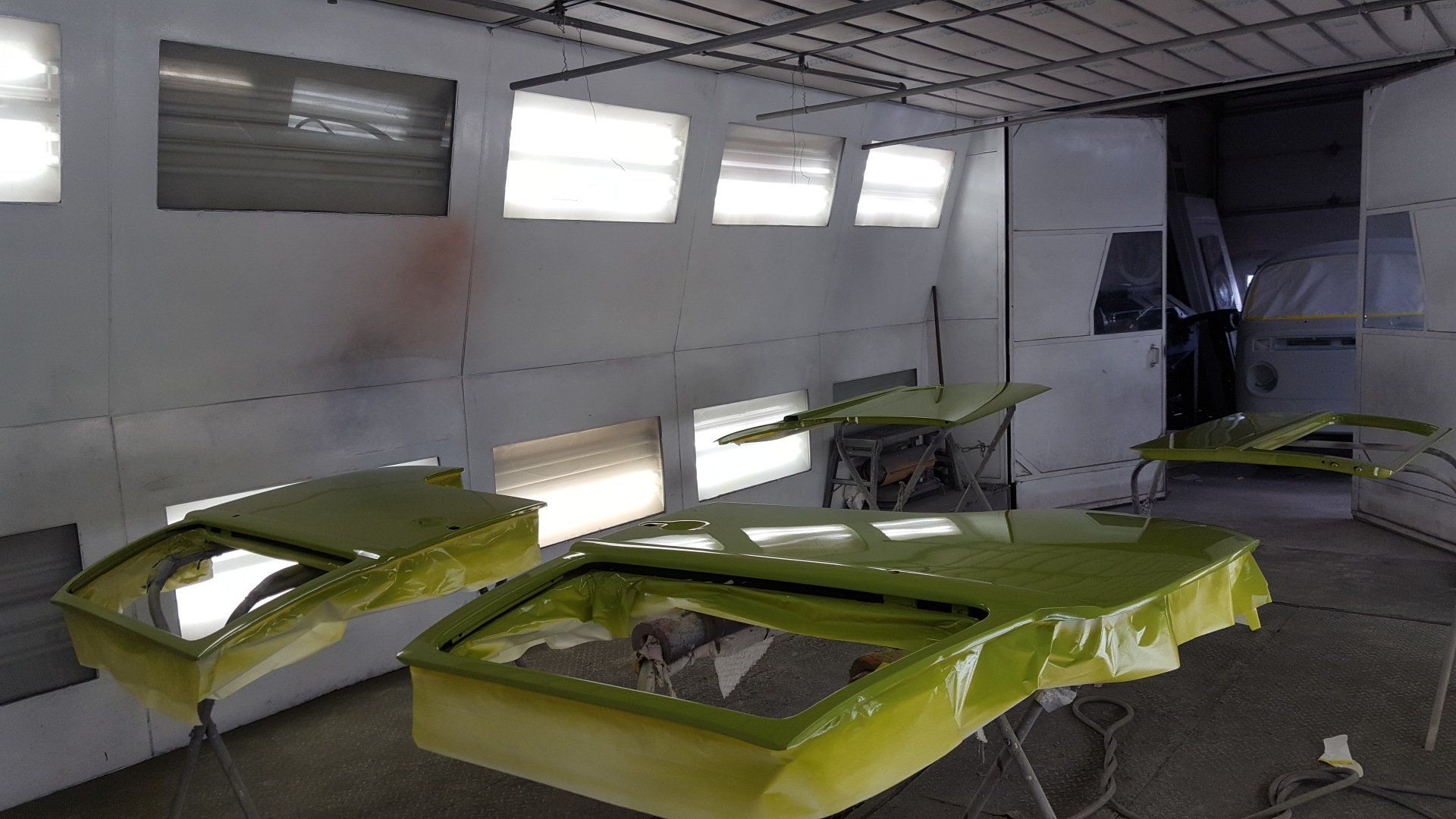 Green car parts in a paint booth. Protective tape, lighting, and workspace.