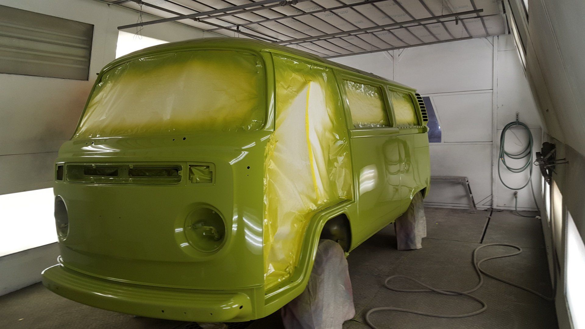 A green Volkswagen bus being painted in a spray booth.