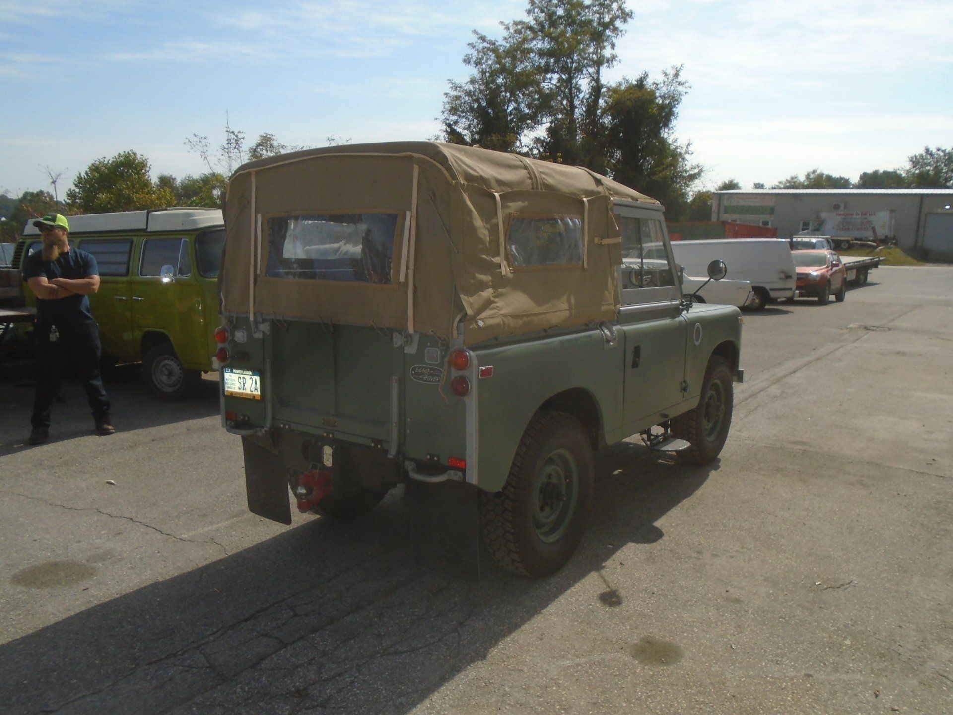 Green Land Rover with tan soft top in a parking lot.