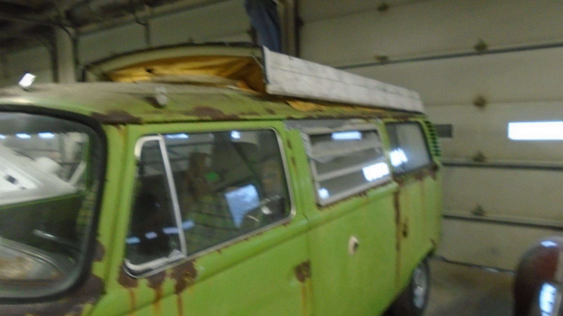 Green, rusty Volkswagen van with a pop-up roof in a garage.