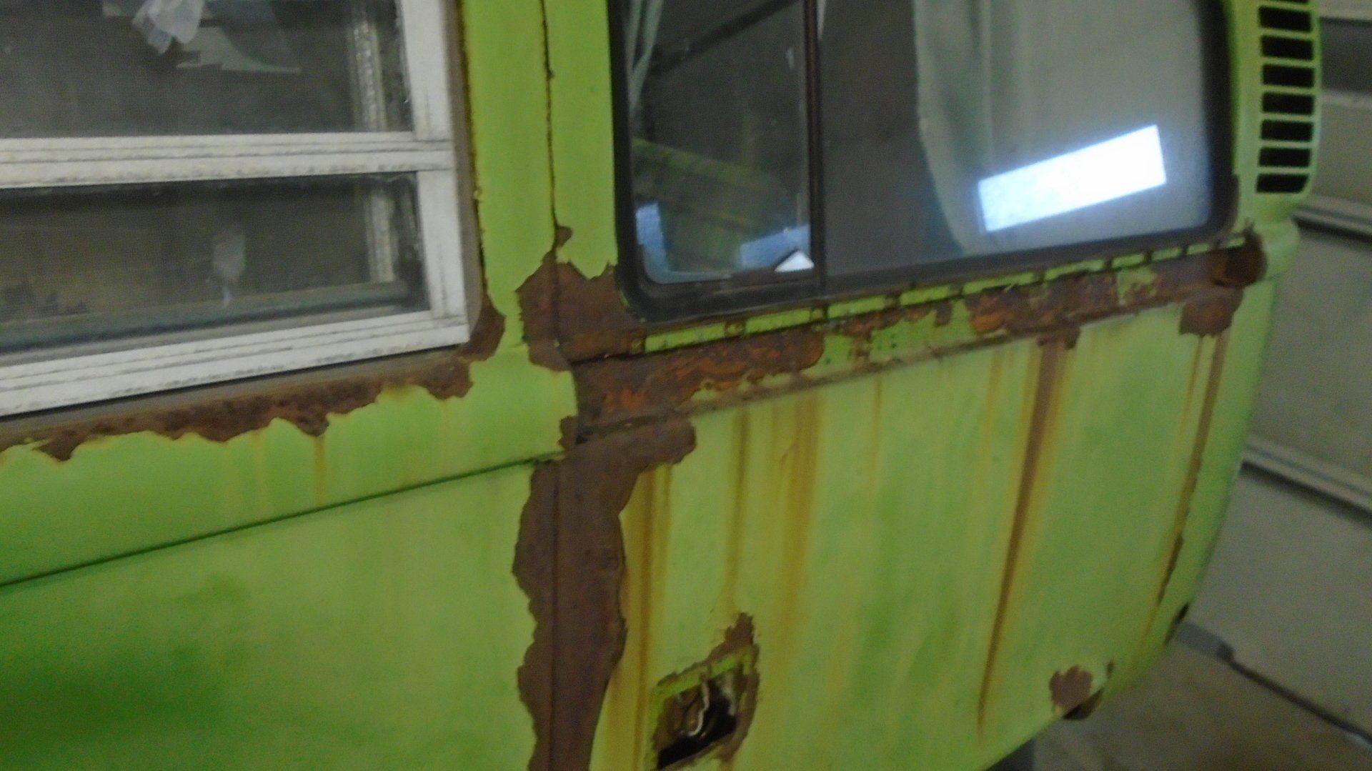 Green vehicle body with extensive rust damage near windows and door.