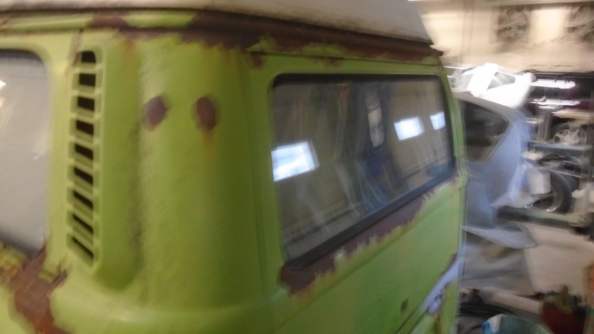 Green and rusty Volkswagen bus side with window and ventilation slats.