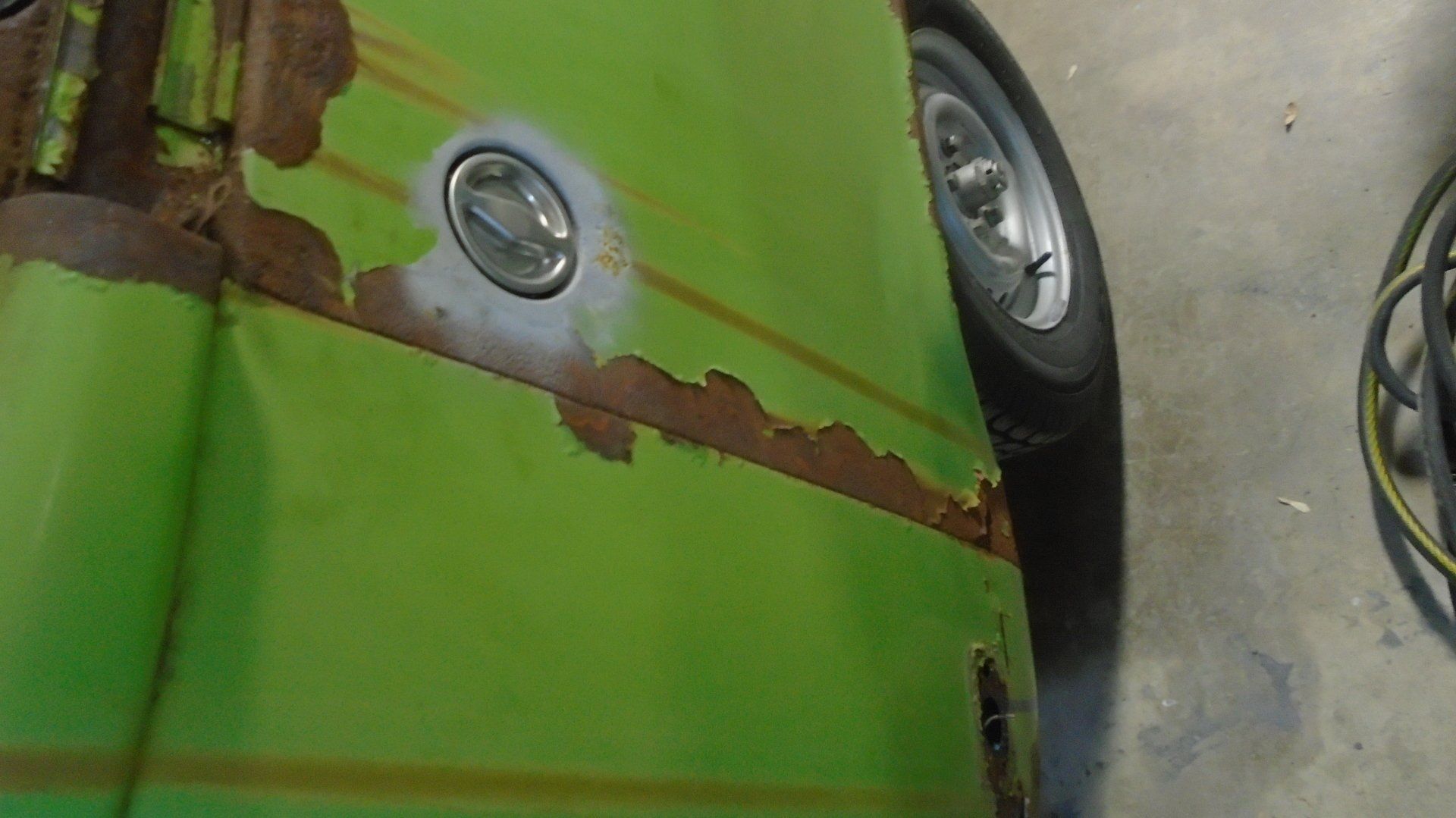 Green car door with severe rust damage around the fuel cap and along the side.