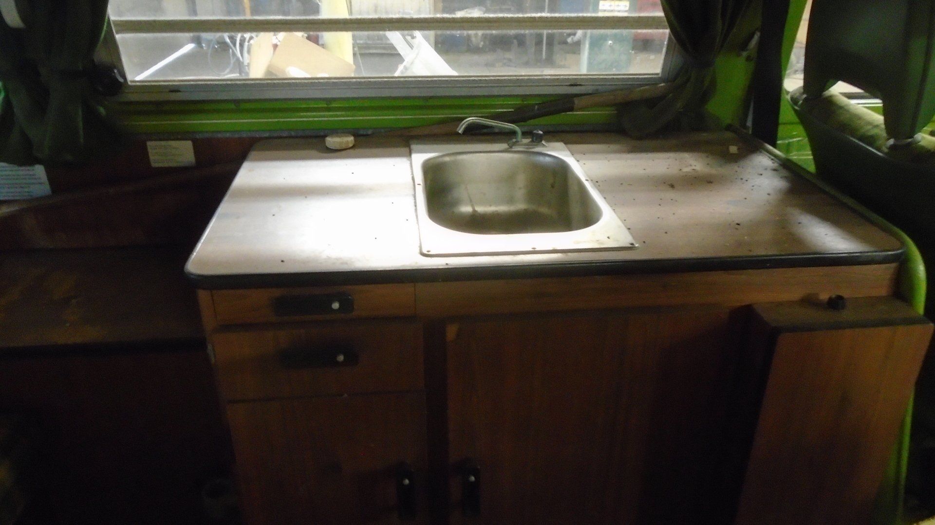 Interior shot of a camper with a sink, counter, cabinets, and a window in the background.