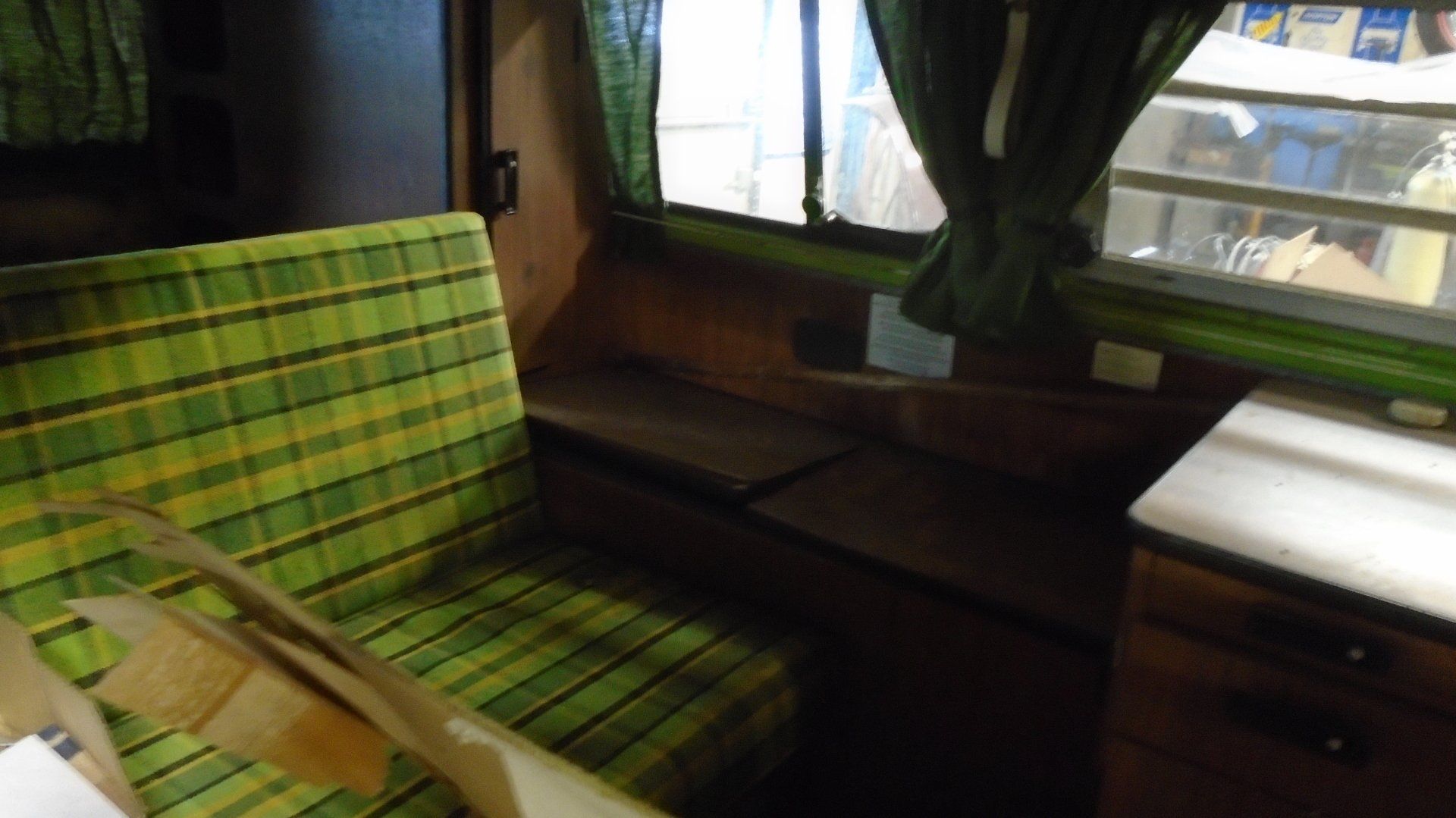 Interior of a green and brown camper van with plaid seating, curtains, and cabinets.