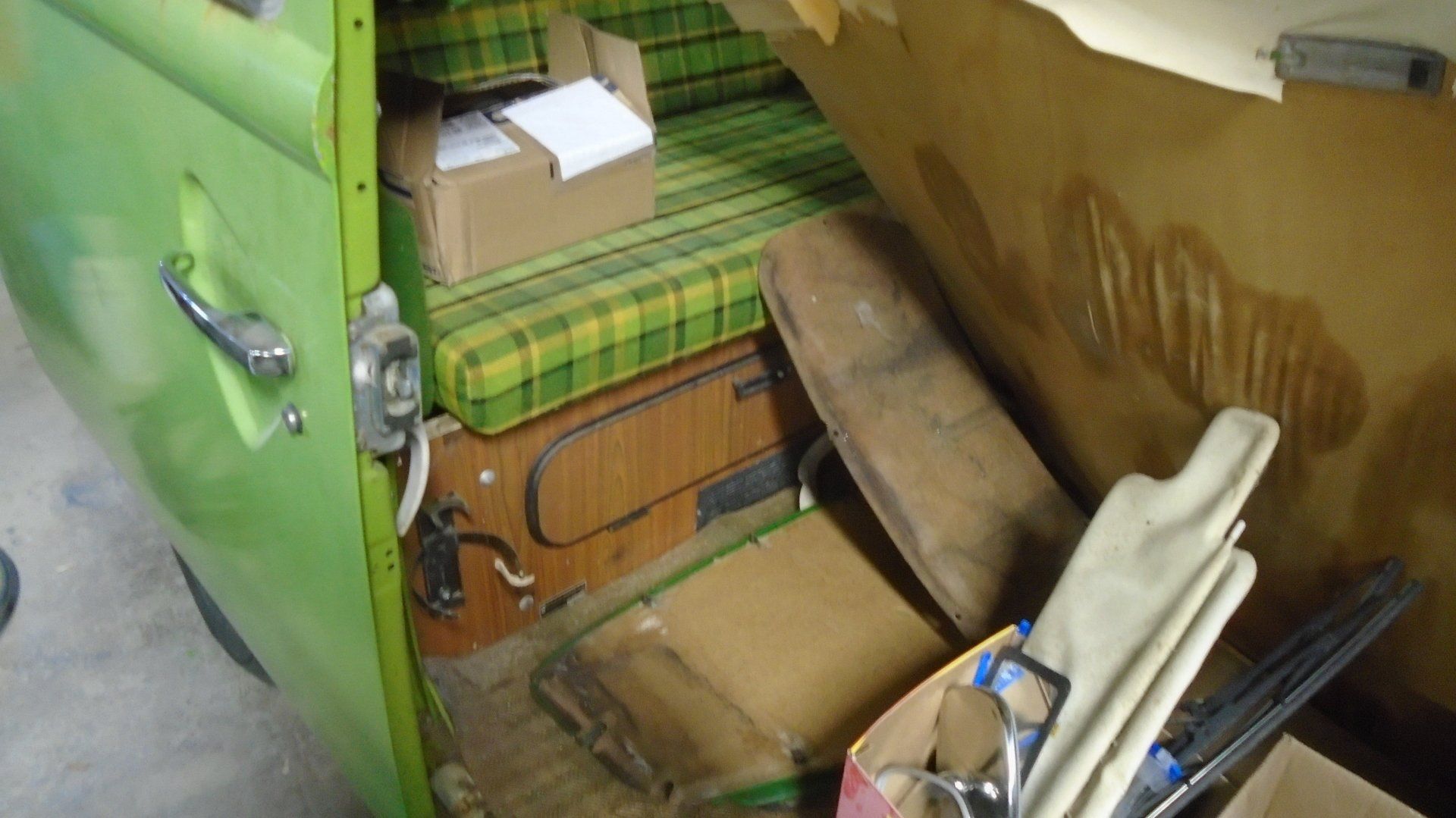 Green van interior showing bench seat with plaid fabric, open door, and scattered items.