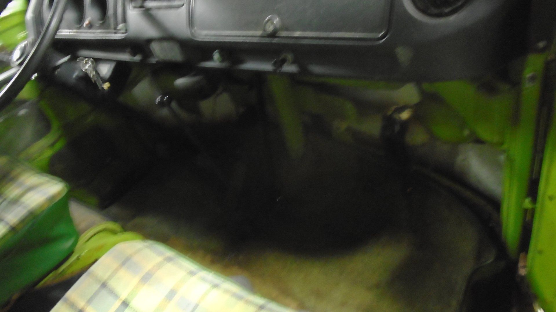 Interior of a green and white Volkswagen van. Black dashboard, dark floor, checkered seat visible.