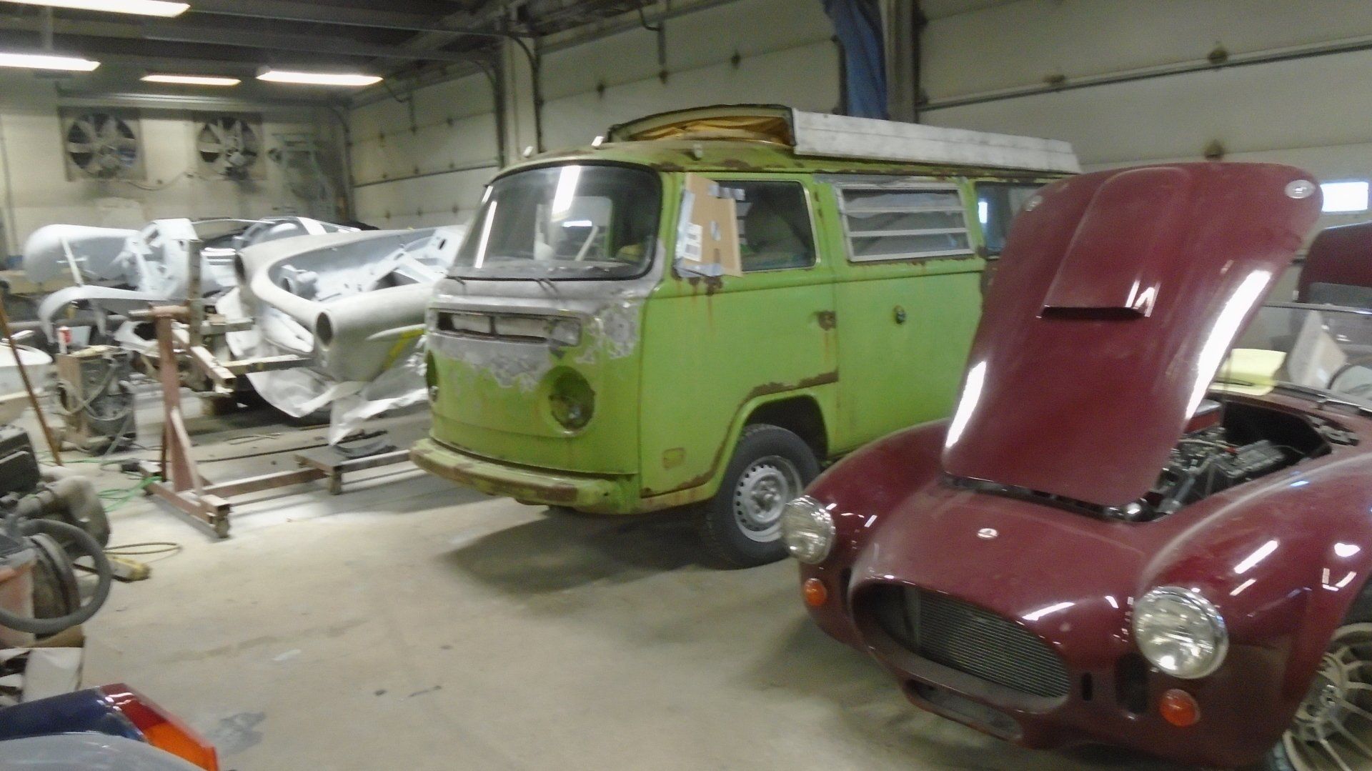 A garage with a green VW bus, a red sports car, and car parts in the background.