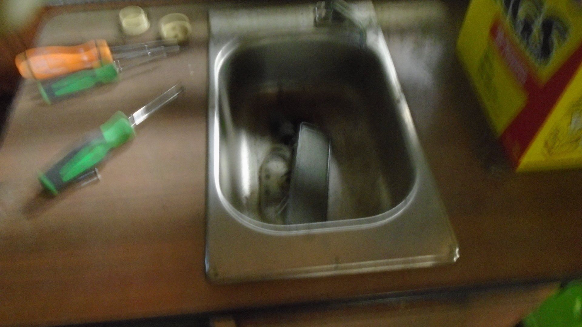 Stainless steel sink with screwdrivers and parts on a wooden surface.