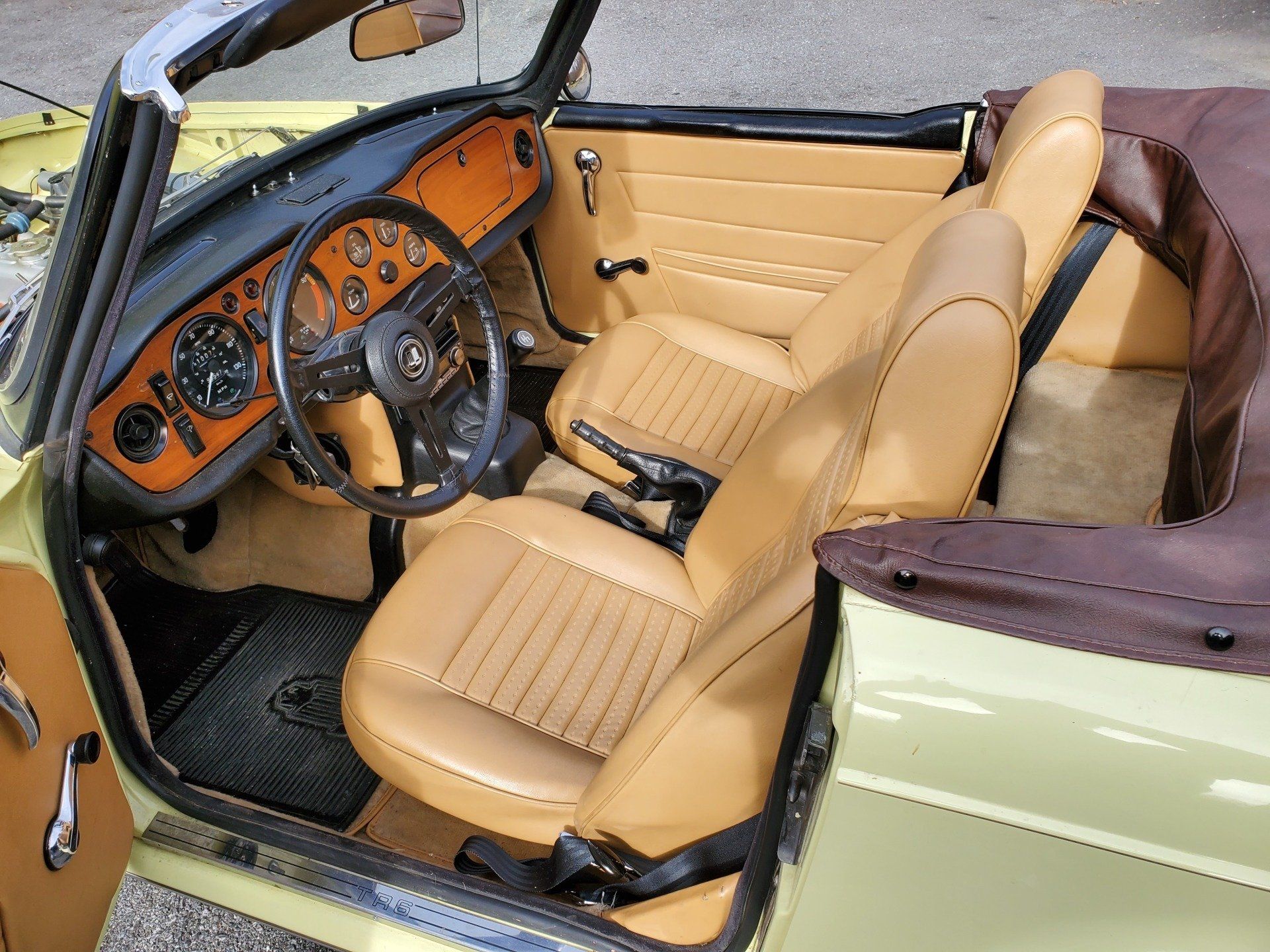 Interior view of a light yellow convertible with tan seats, a black dashboard, and a brown convertible top.