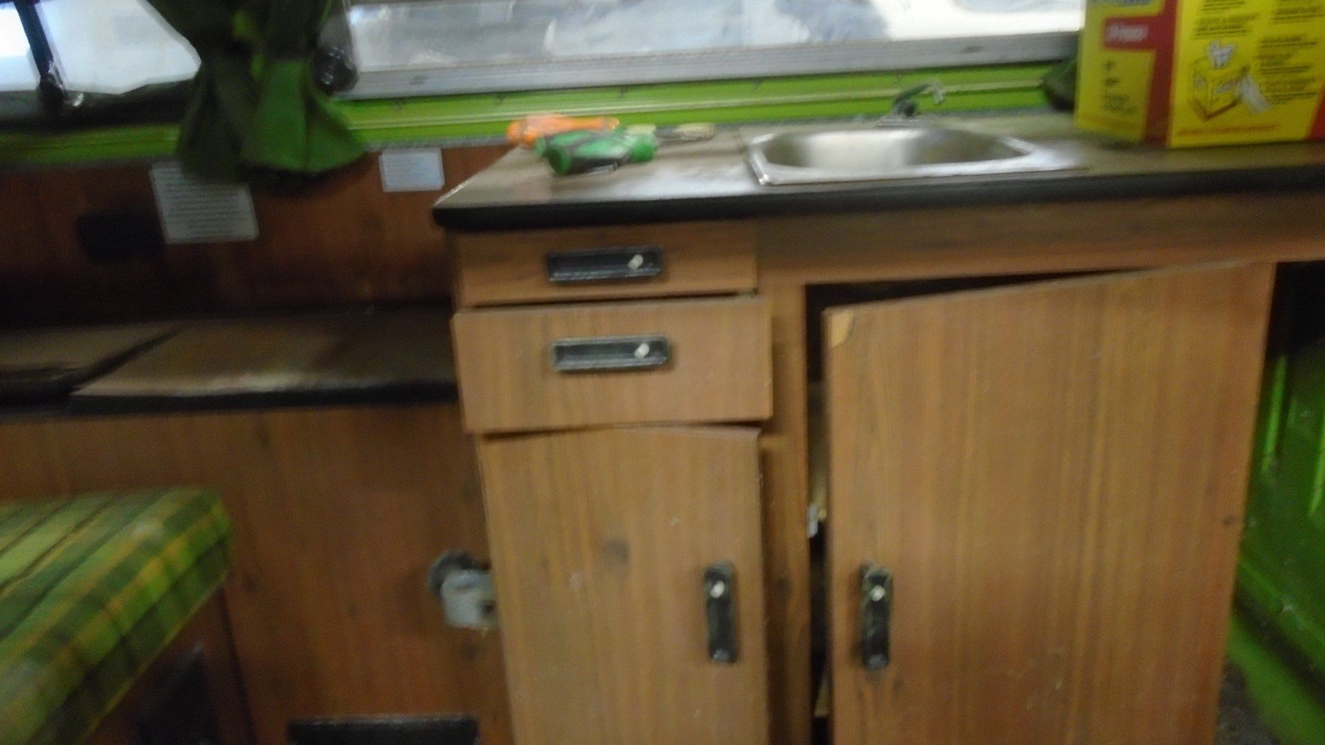 Interior camper with wooden cabinets, sink, and open door. Green and tan tones throughout.