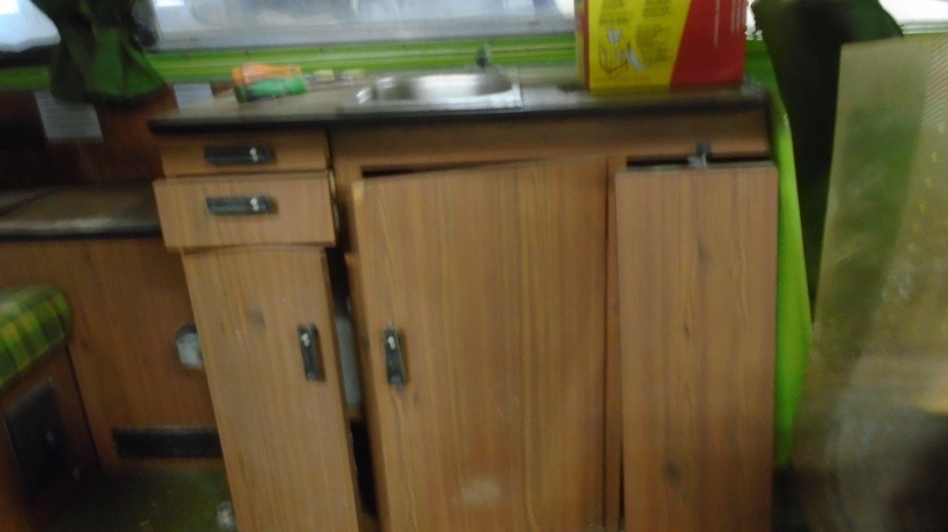 Interior of a camper with a wooden cabinet and sink; the door of the cabinet is slightly ajar.
