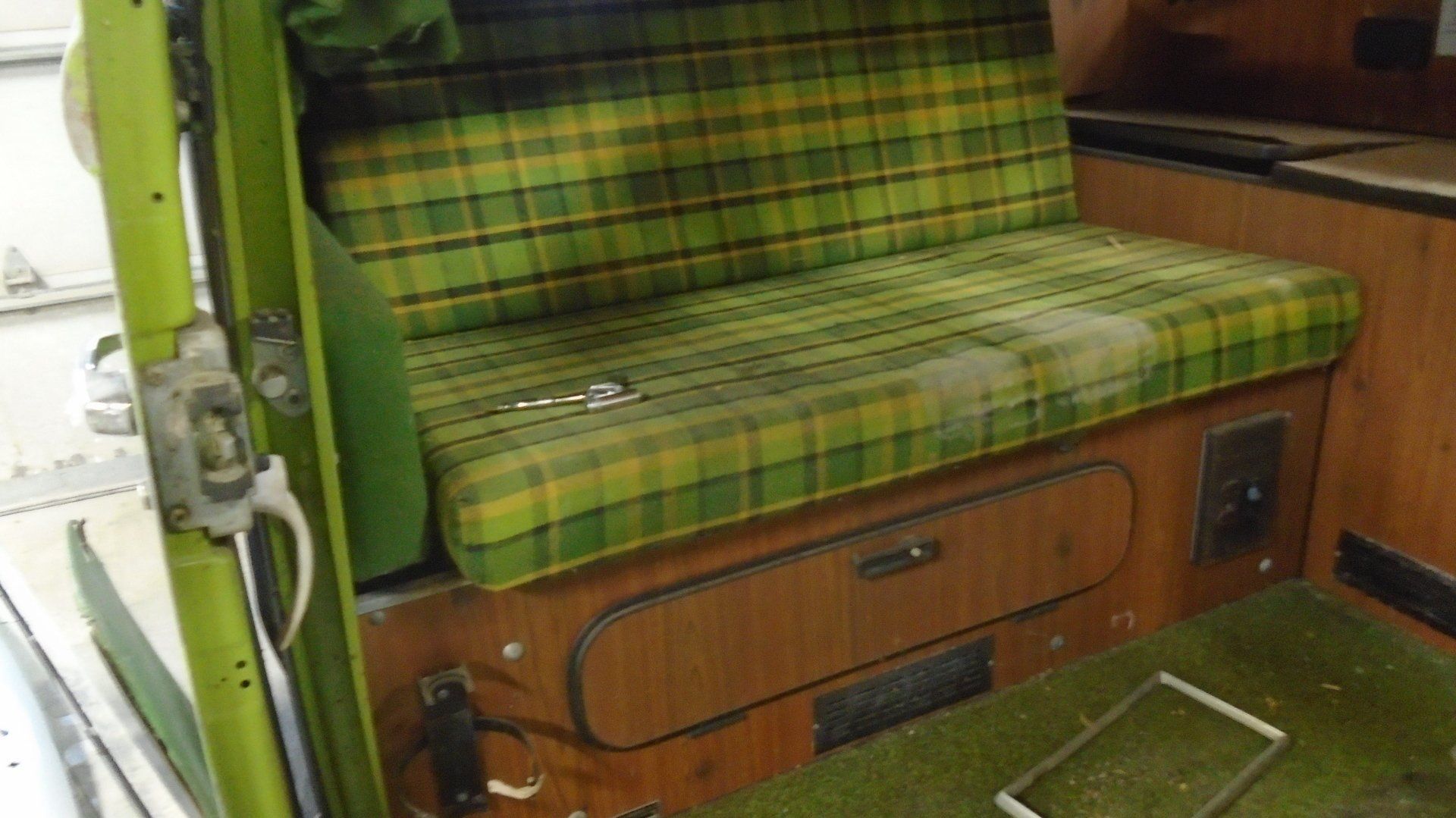 Interior of a vintage van with a plaid green bench seat and wood paneling.
