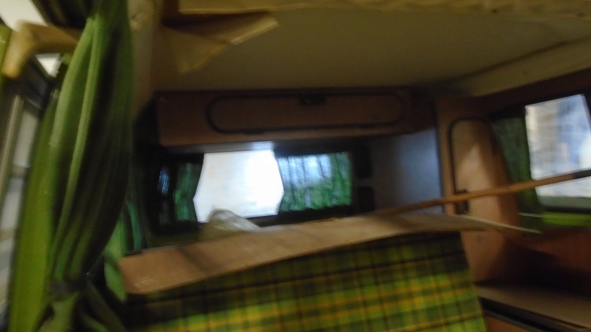 Interior of a camper van with green curtains, plaid fabric, and a wooden shelf.