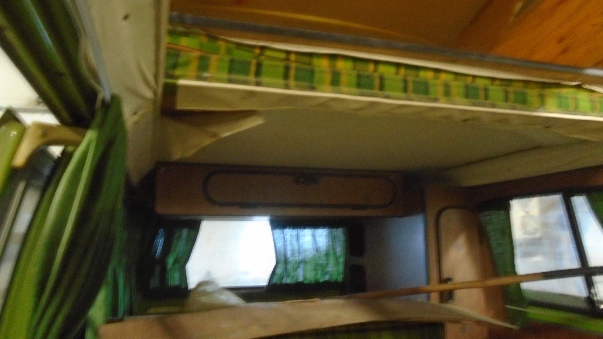 Interior of a camper van with overhead bed, green curtains, and wooden cabinets.