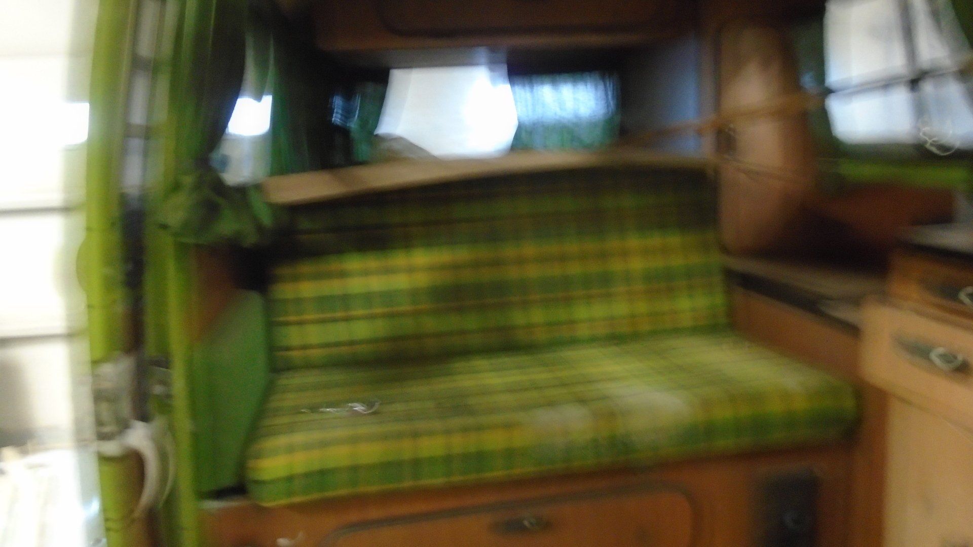 Interior of a van with a green and yellow plaid seat, wood cabinets, and green curtains.