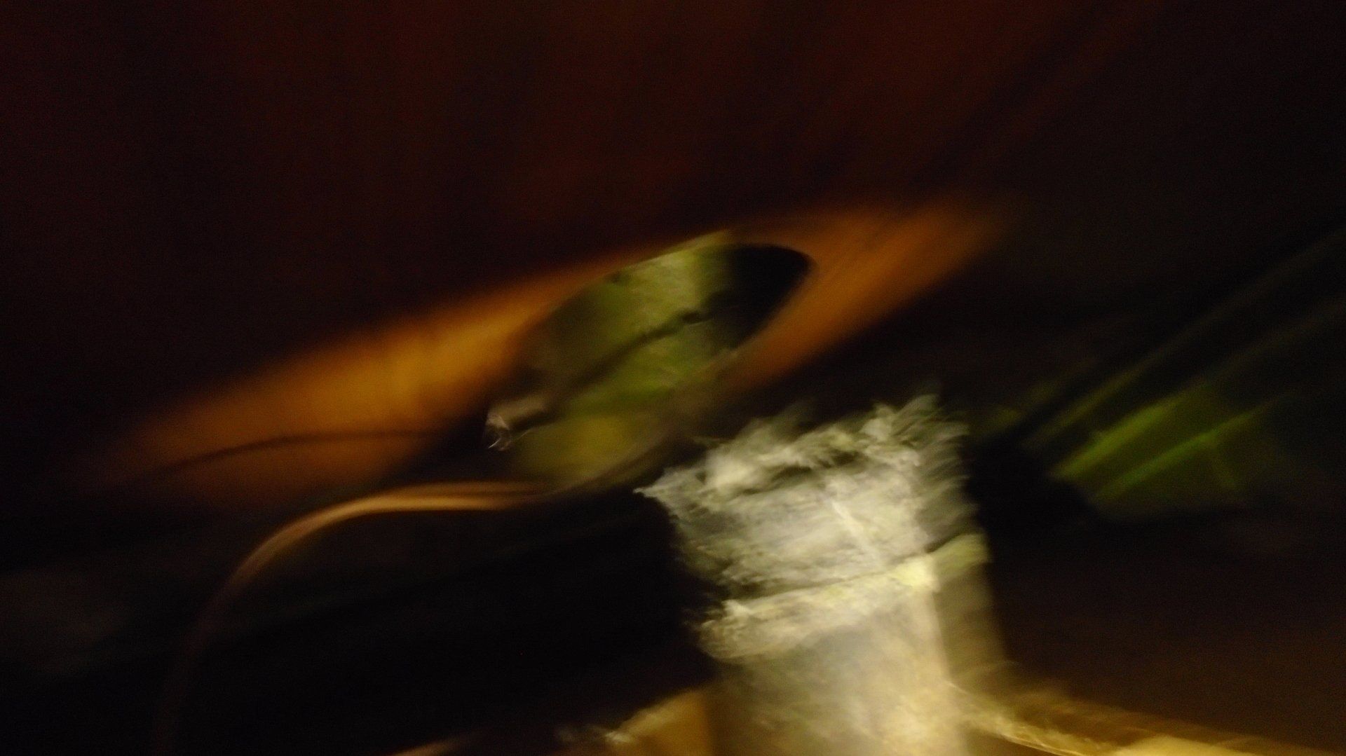 Dark and blurry: A light-colored object, possibly a bottle, against dark brown and yellow.