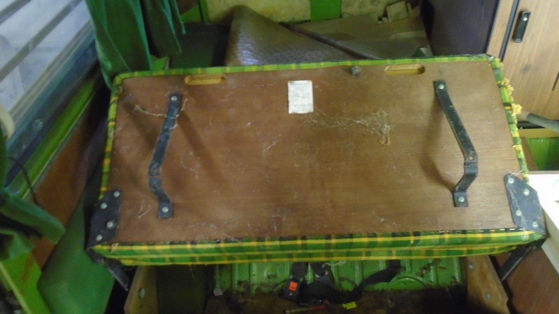 Brown wooden chest with black handles and green plaid trim.