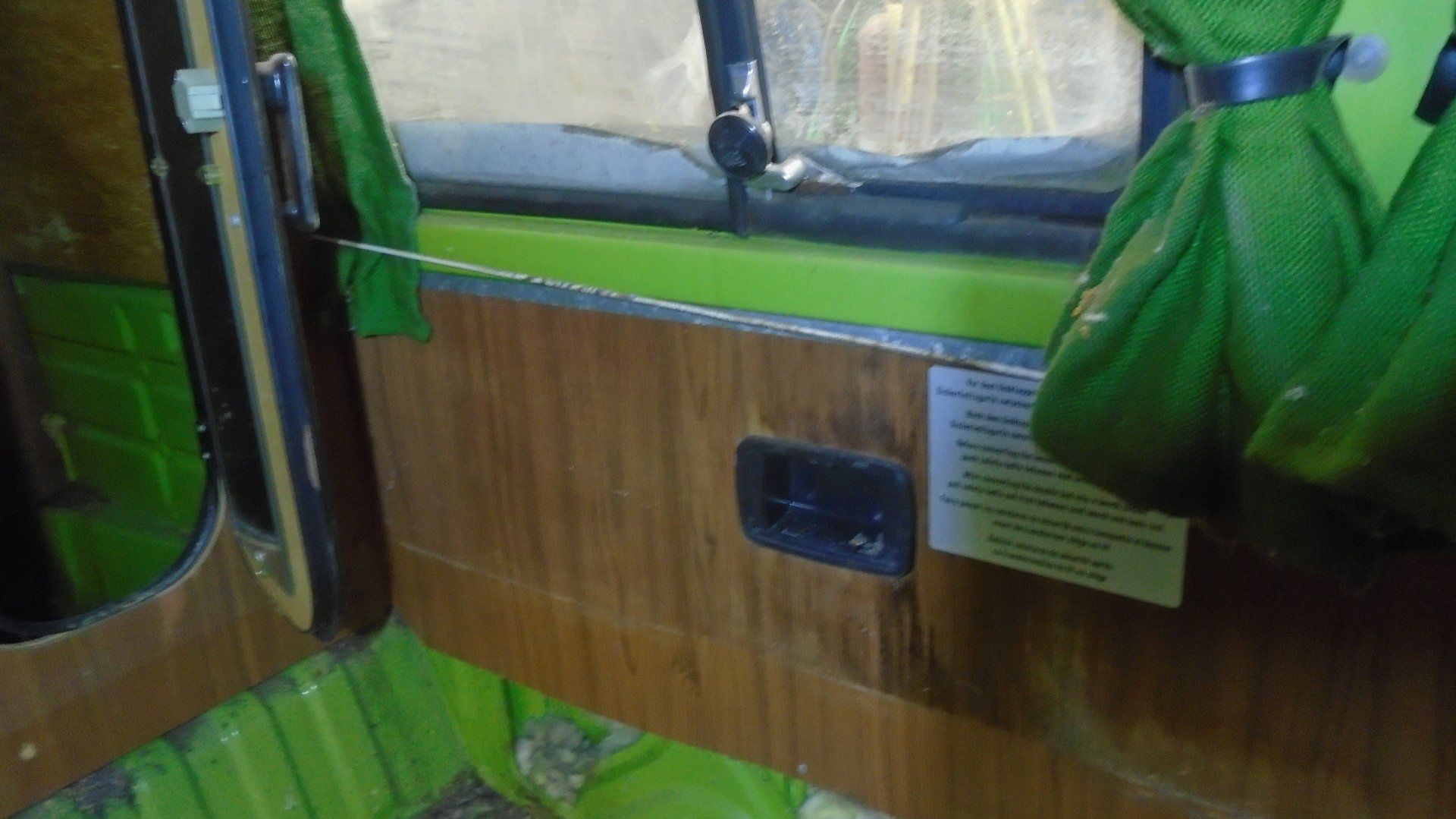 Interior view of a vehicle door, featuring wood paneling, green trim, a window, and a door handle.