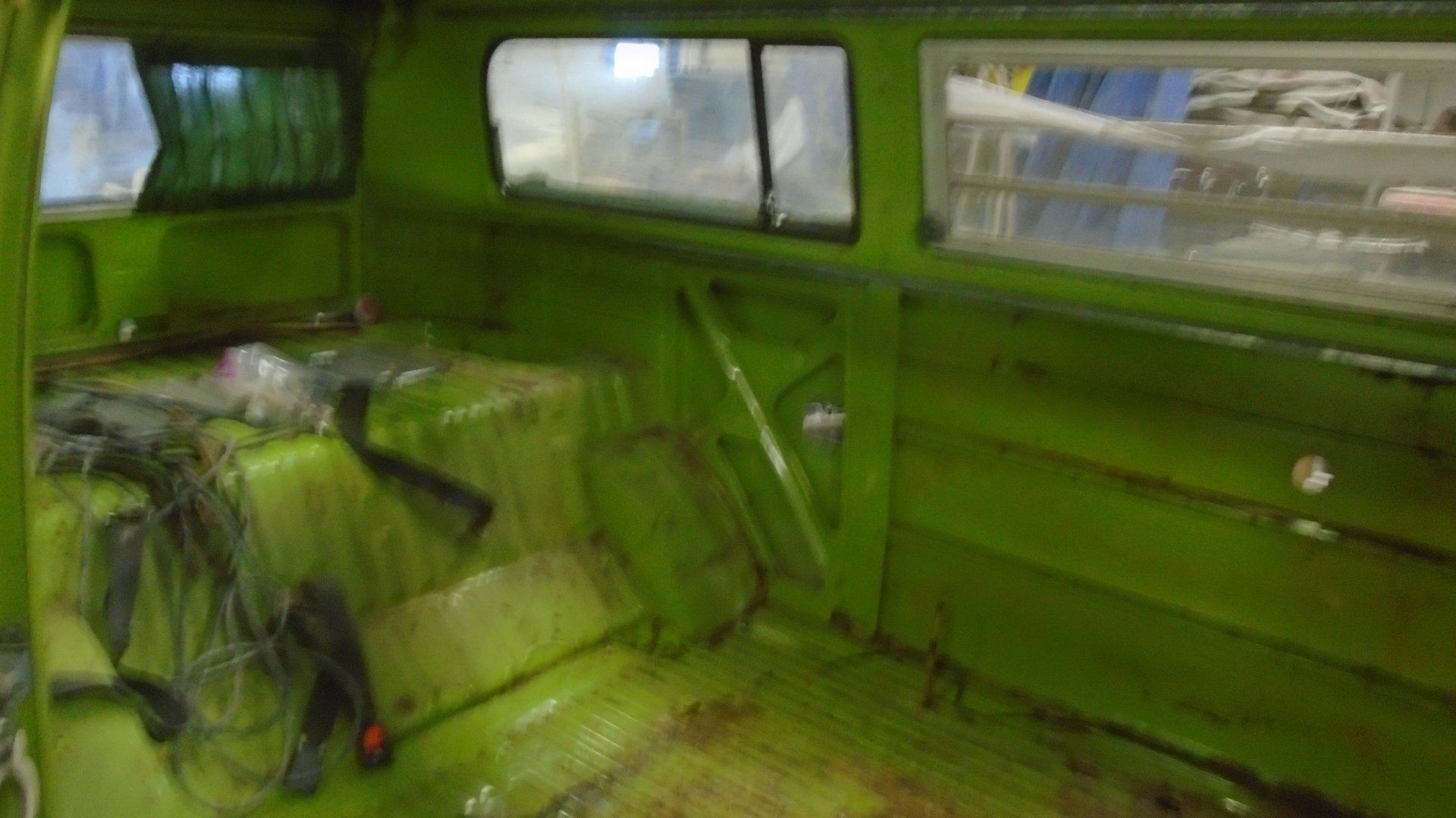 Interior of a green van with window frames and exposed metal, wires on floor.