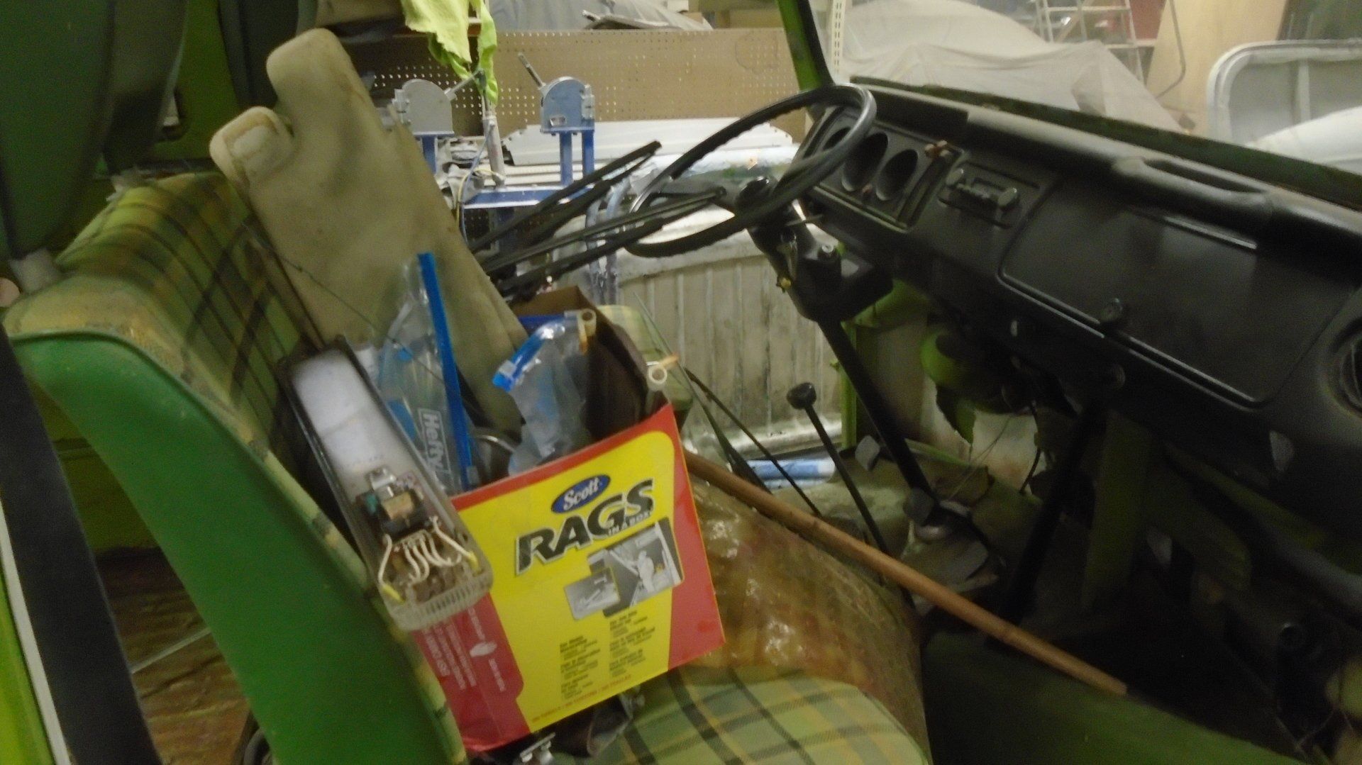 Interior of a green vintage van filled with items, including a box of rags and an oven mitt, with the steering wheel visible.