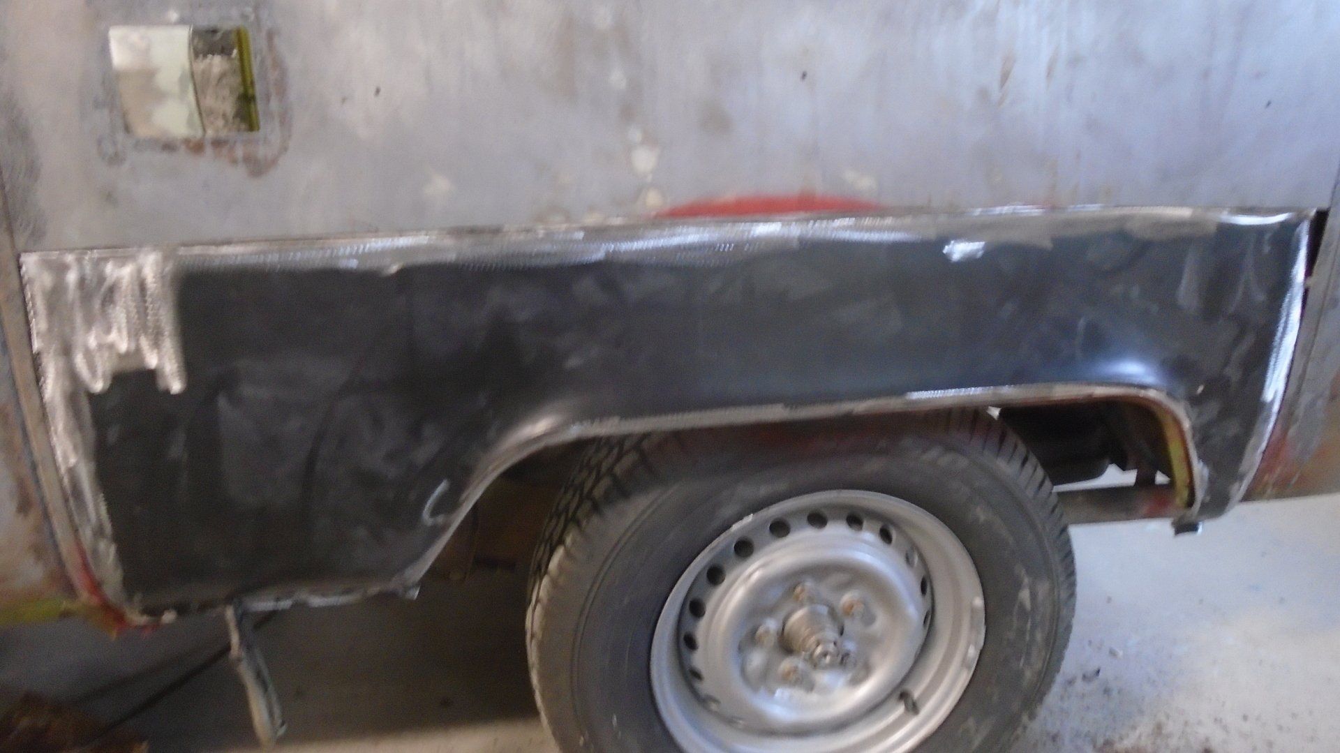 Black car bodywork with a tire and wheel. Body panel repair in progress, with welding and primer visible.