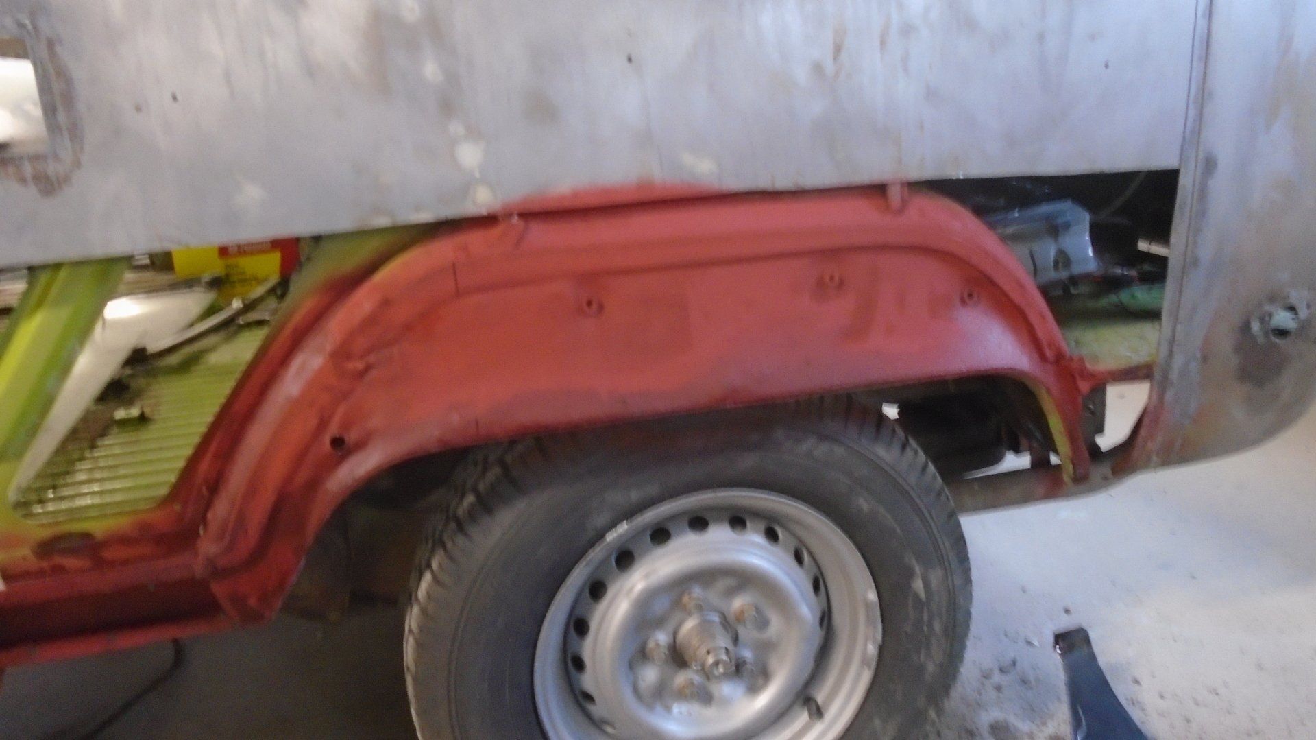 Red car wheel well and tire. Metal body panels in process of repair.