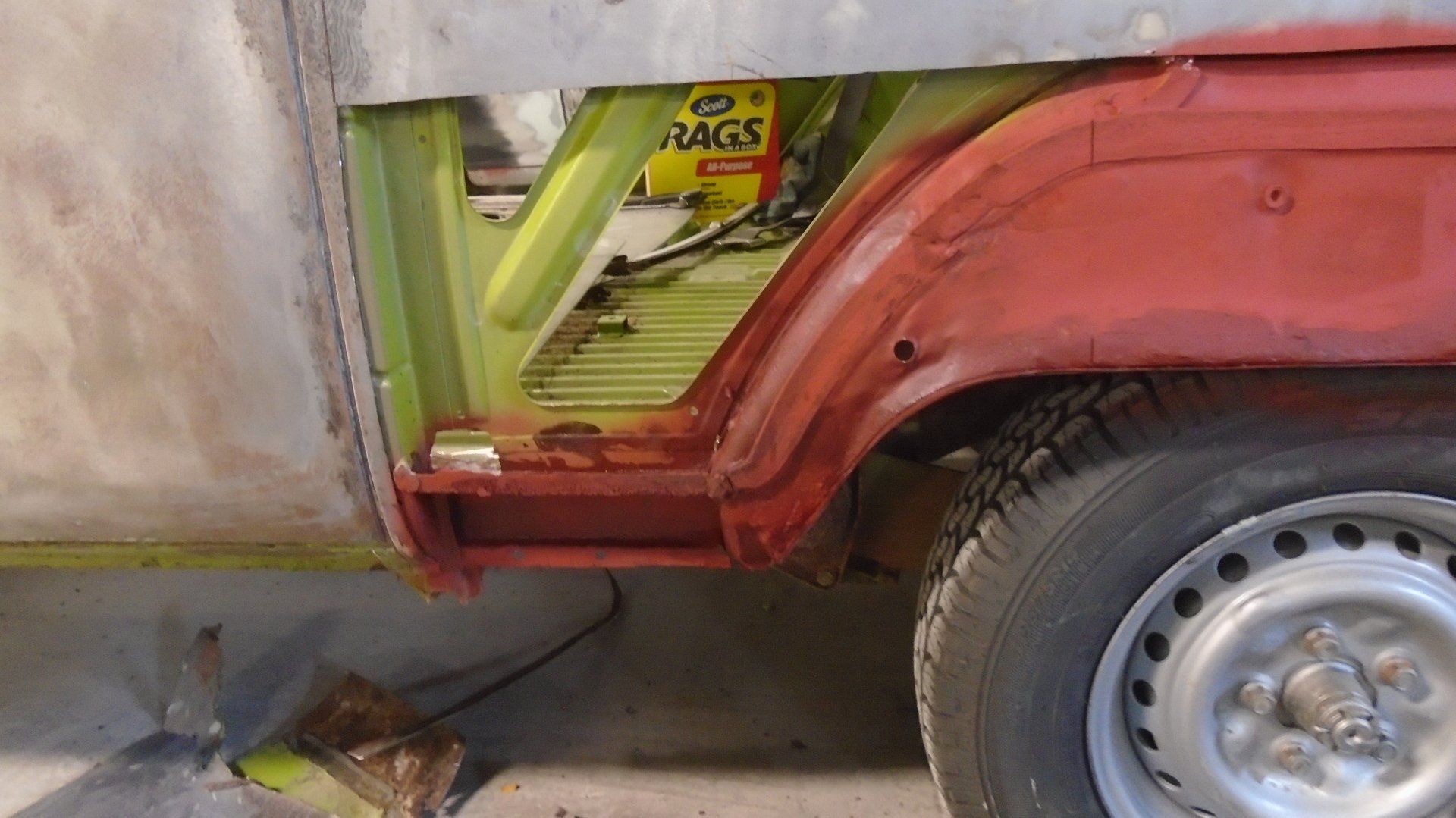 Car body repair in progress; red quarter panel, exposed green frame, wheel.