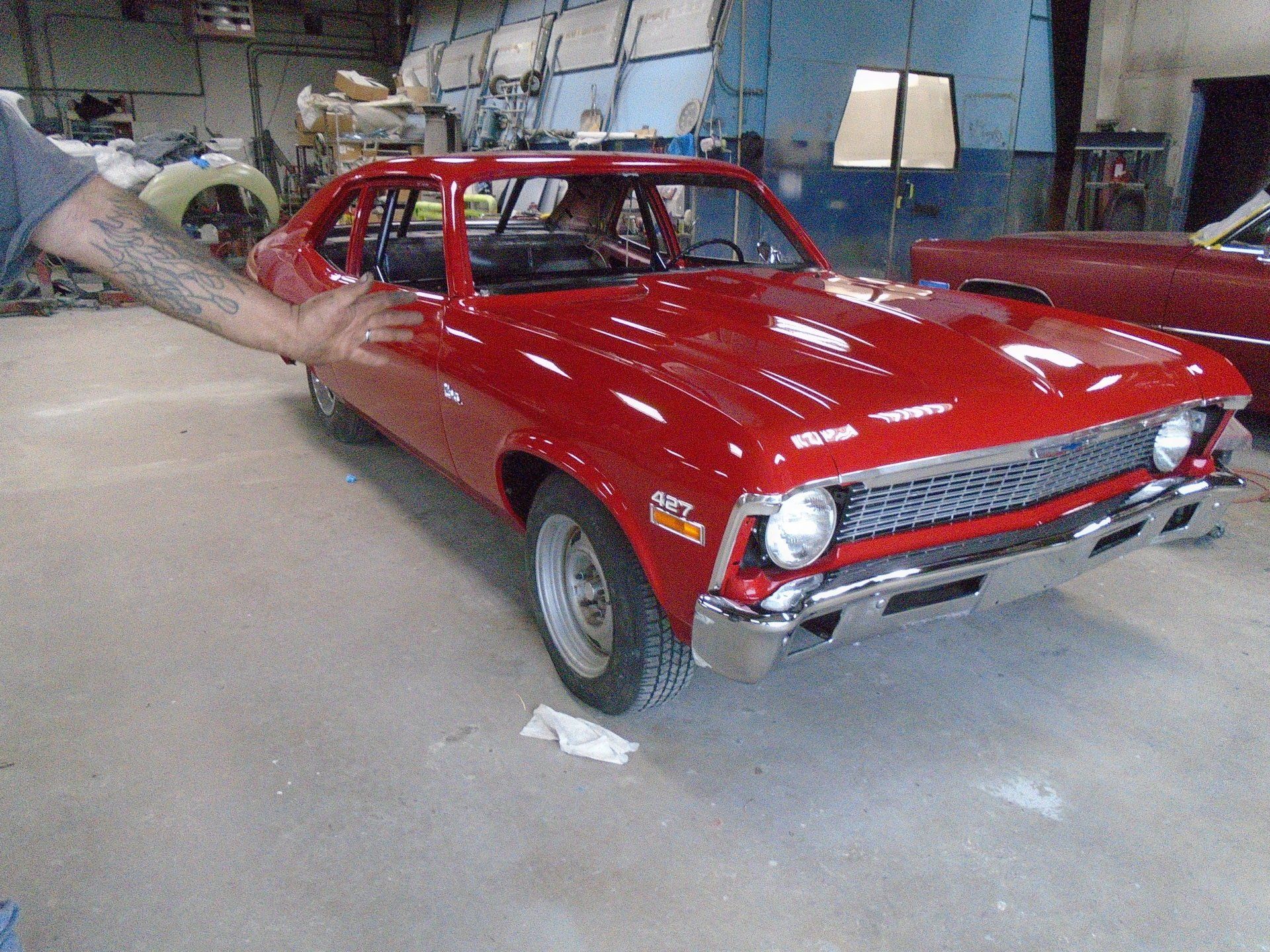 Red classic car being touched by a person's hand in a garage.