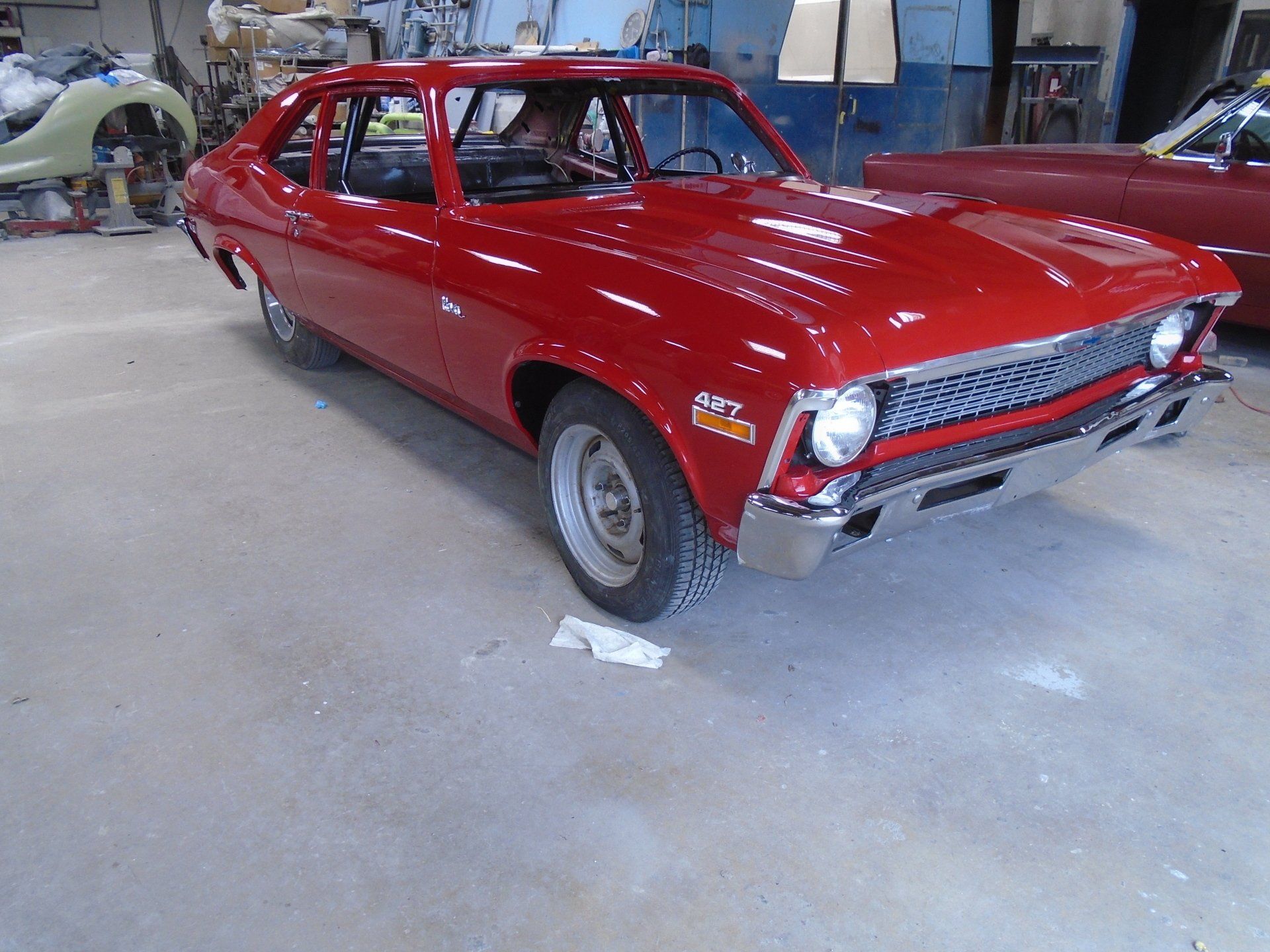 Red vintage Chevy Nova in a garage.