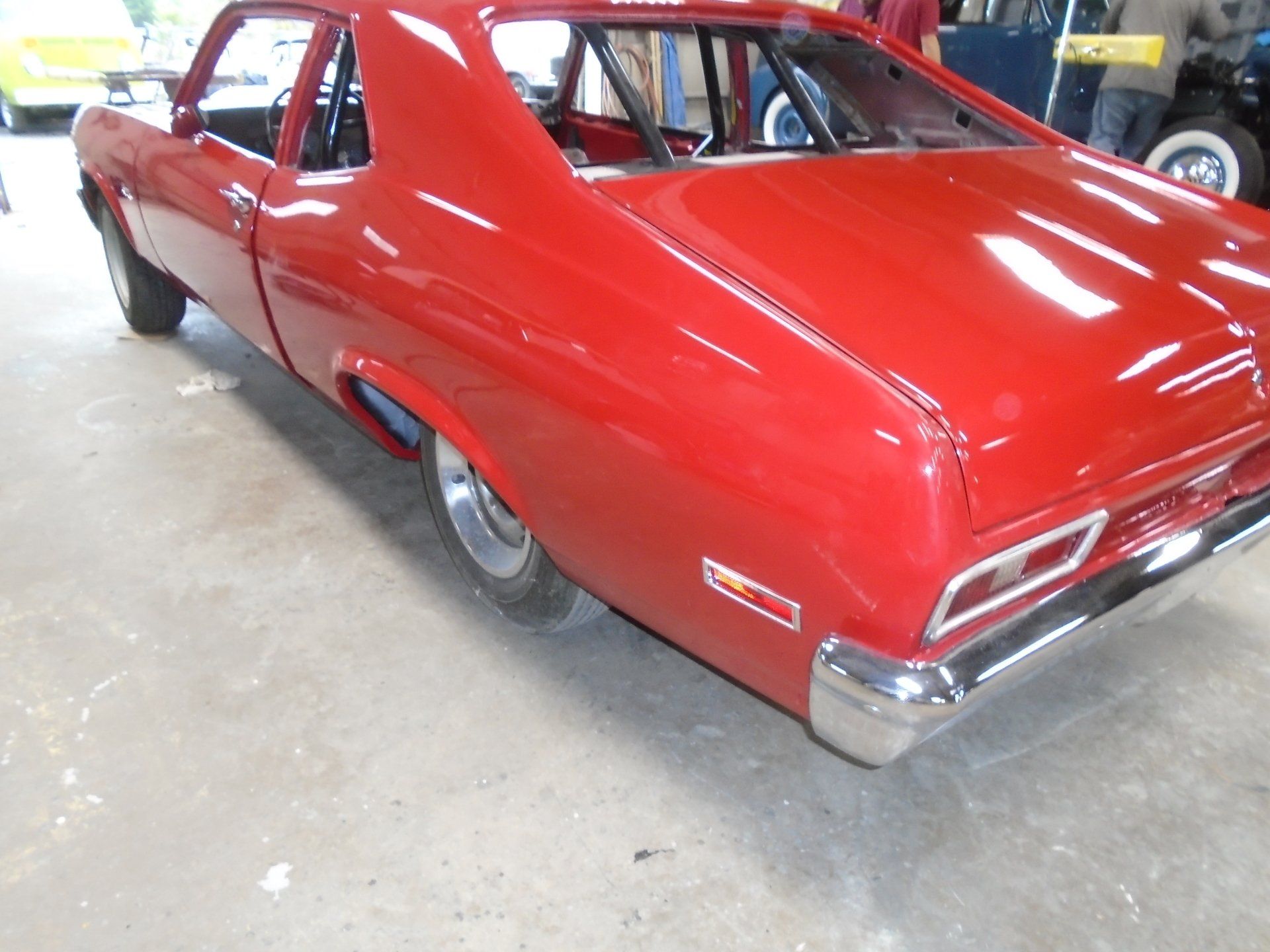 Red classic car, possibly a Chevrolet Nova, with roll cage visible.
