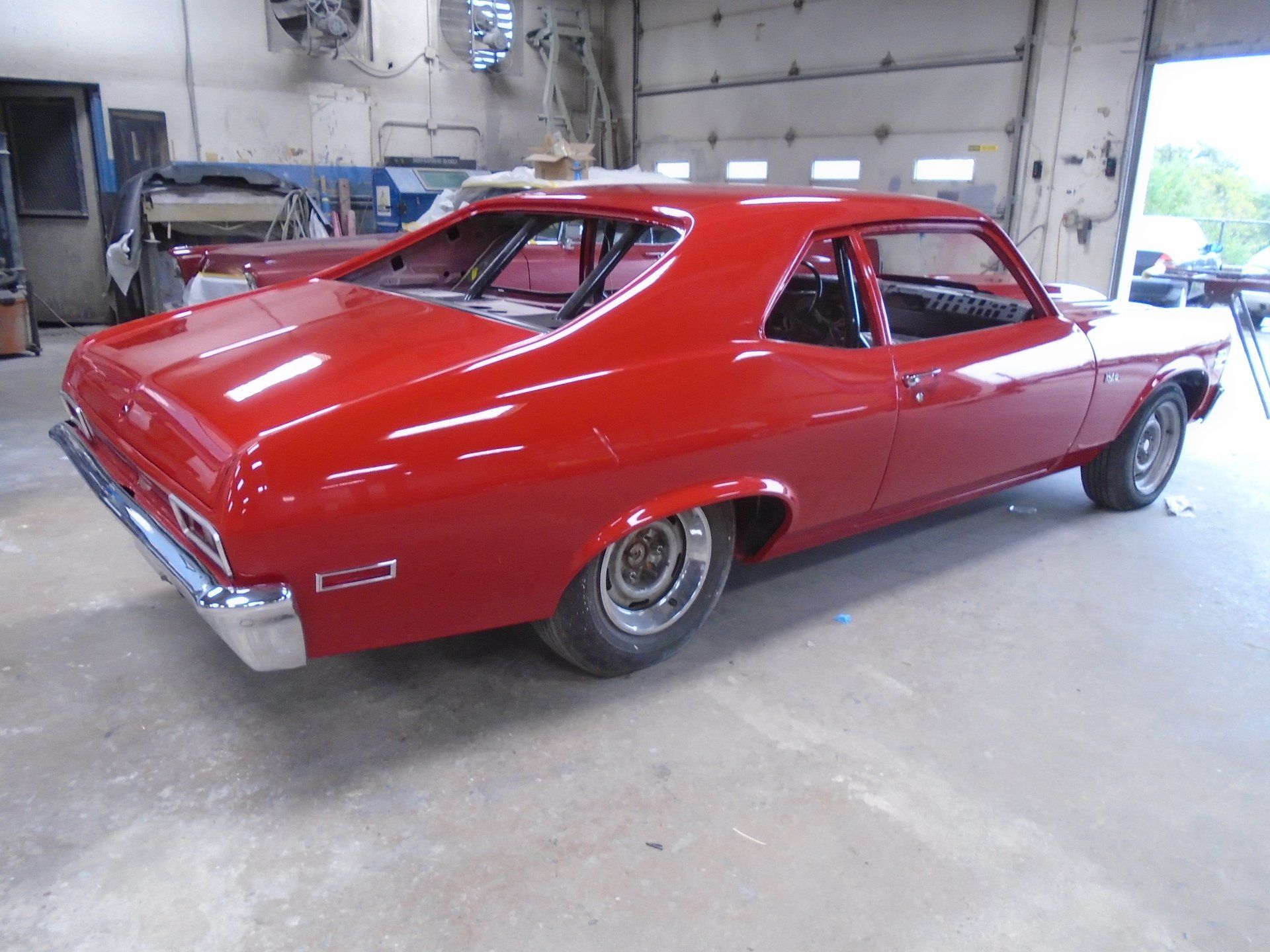 Red classic muscle car in a garage with a roll cage.