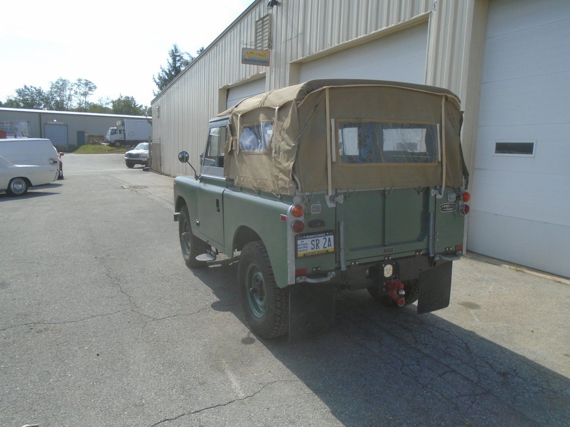 Green Land Rover with a tan canvas top parked in front of a building.