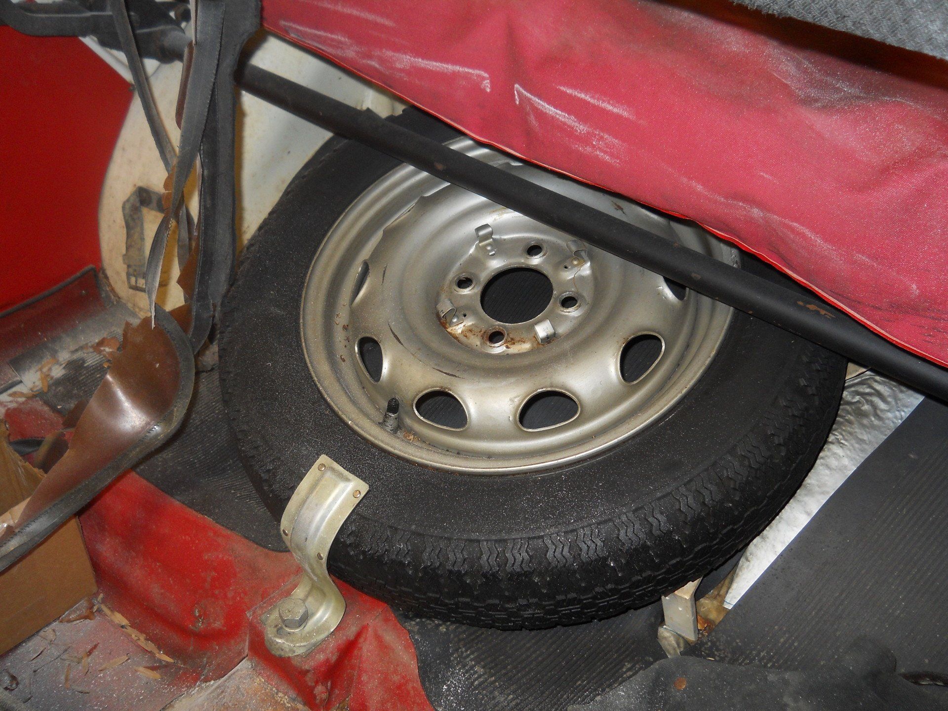 Spare tire in a car trunk, partially covered by red fabric.