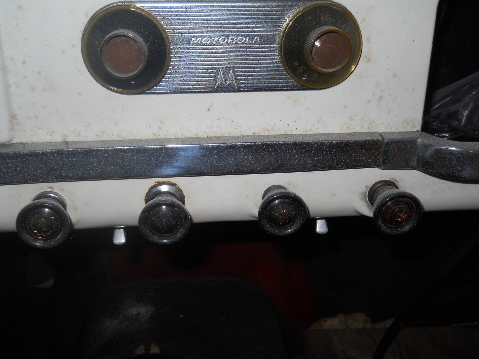 Close-up of a vintage car dashboard with a Motorola radio and multiple knobs on a white surface.