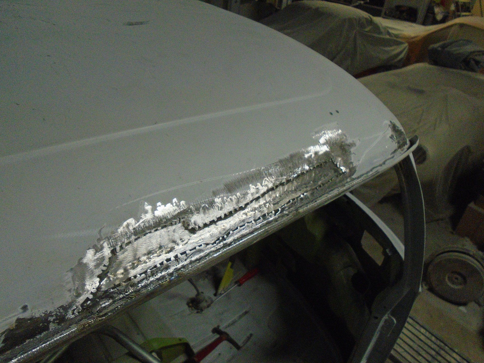 Car roof with extensive rust damage near the seam, in a garage setting.
