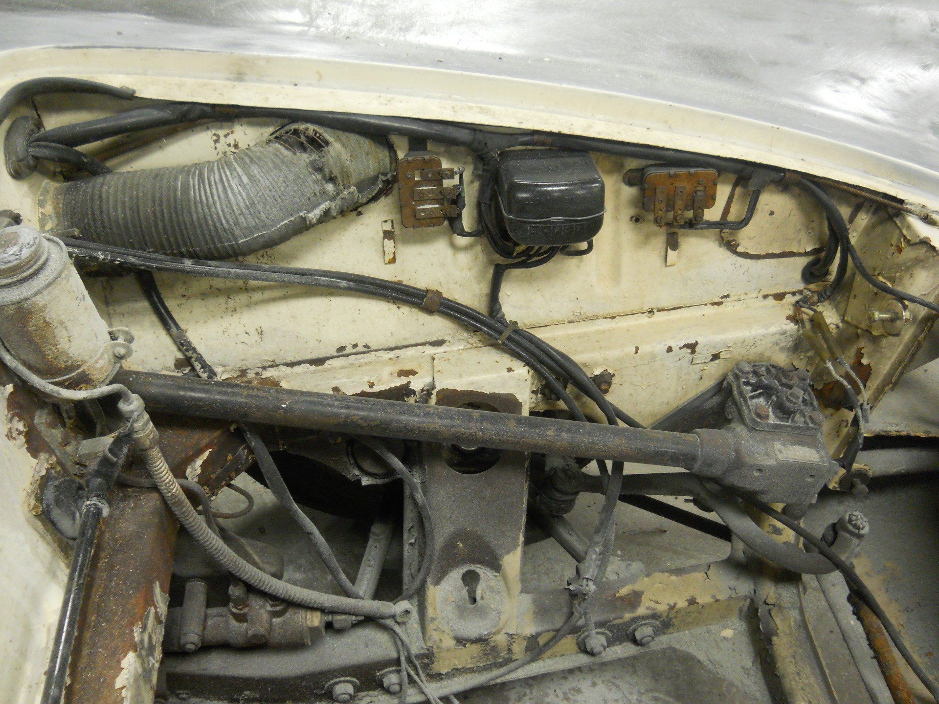 Engine compartment of an old car, showing wires, tubing, and mechanical parts in a dusty, worn condition.