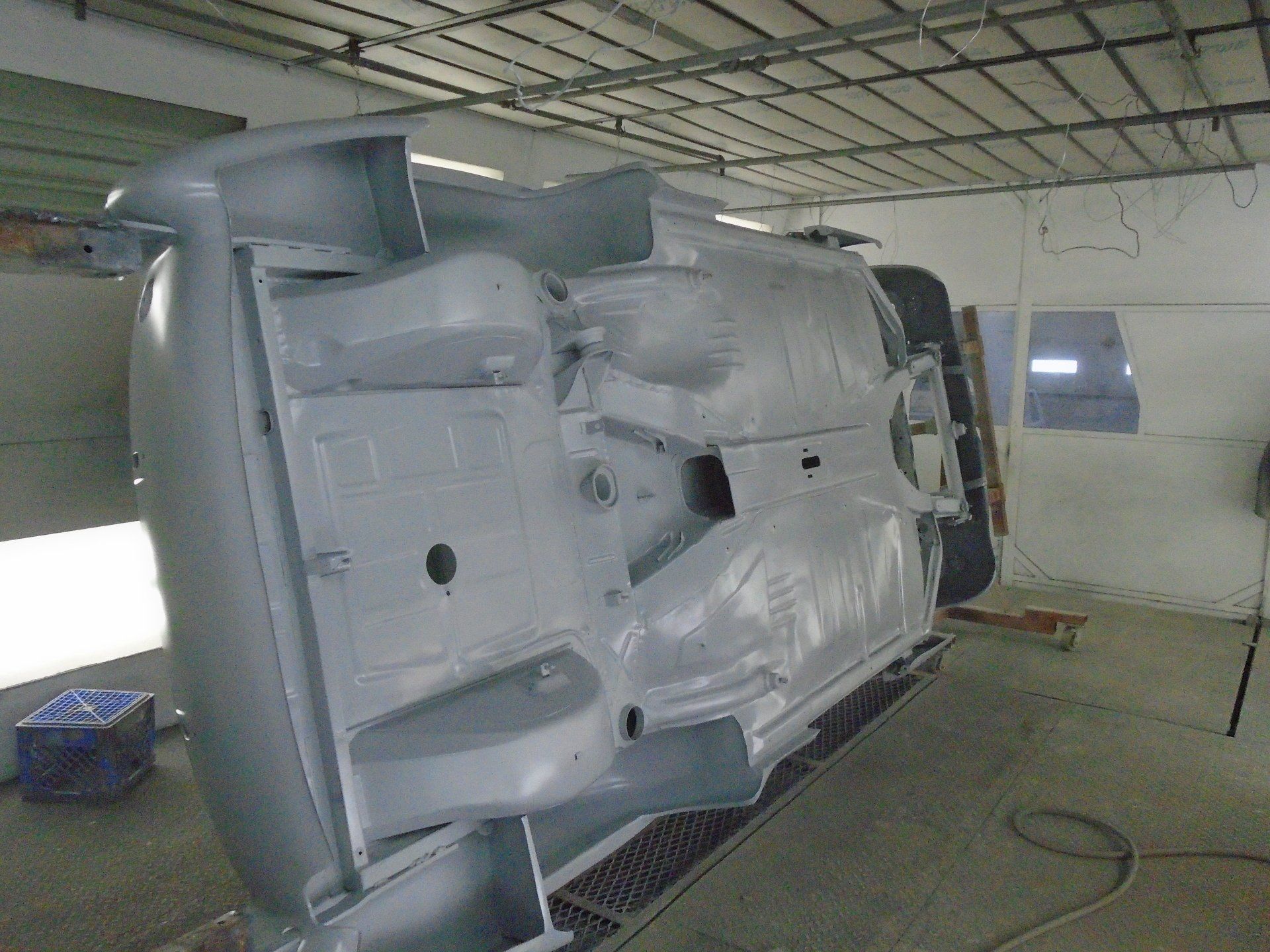 Underside of a car body being painted light gray inside a spray booth.
