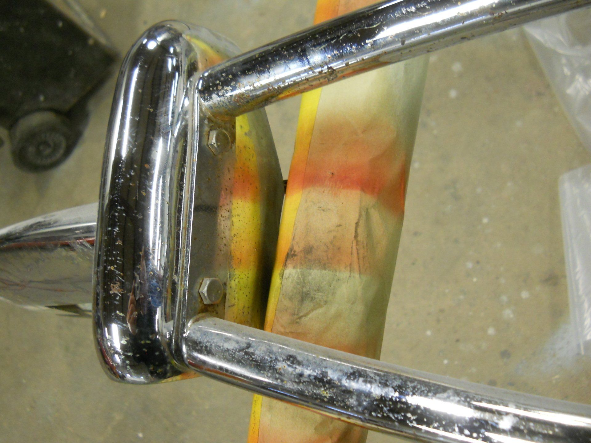 Chrome bumper attached to a multi-colored painted surface with bolts.