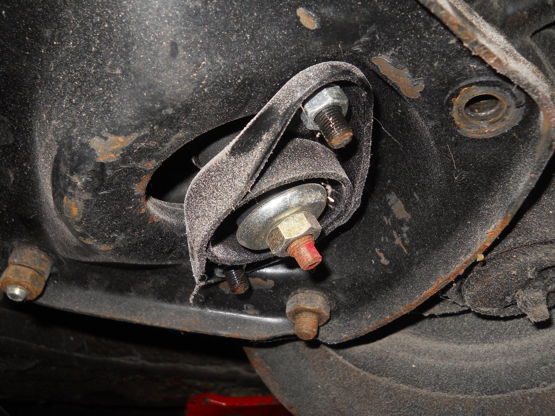 Close-up of a vehicle component. A black, bracket-like structure with bolts, a rubber bushing, and a wrapped strap.