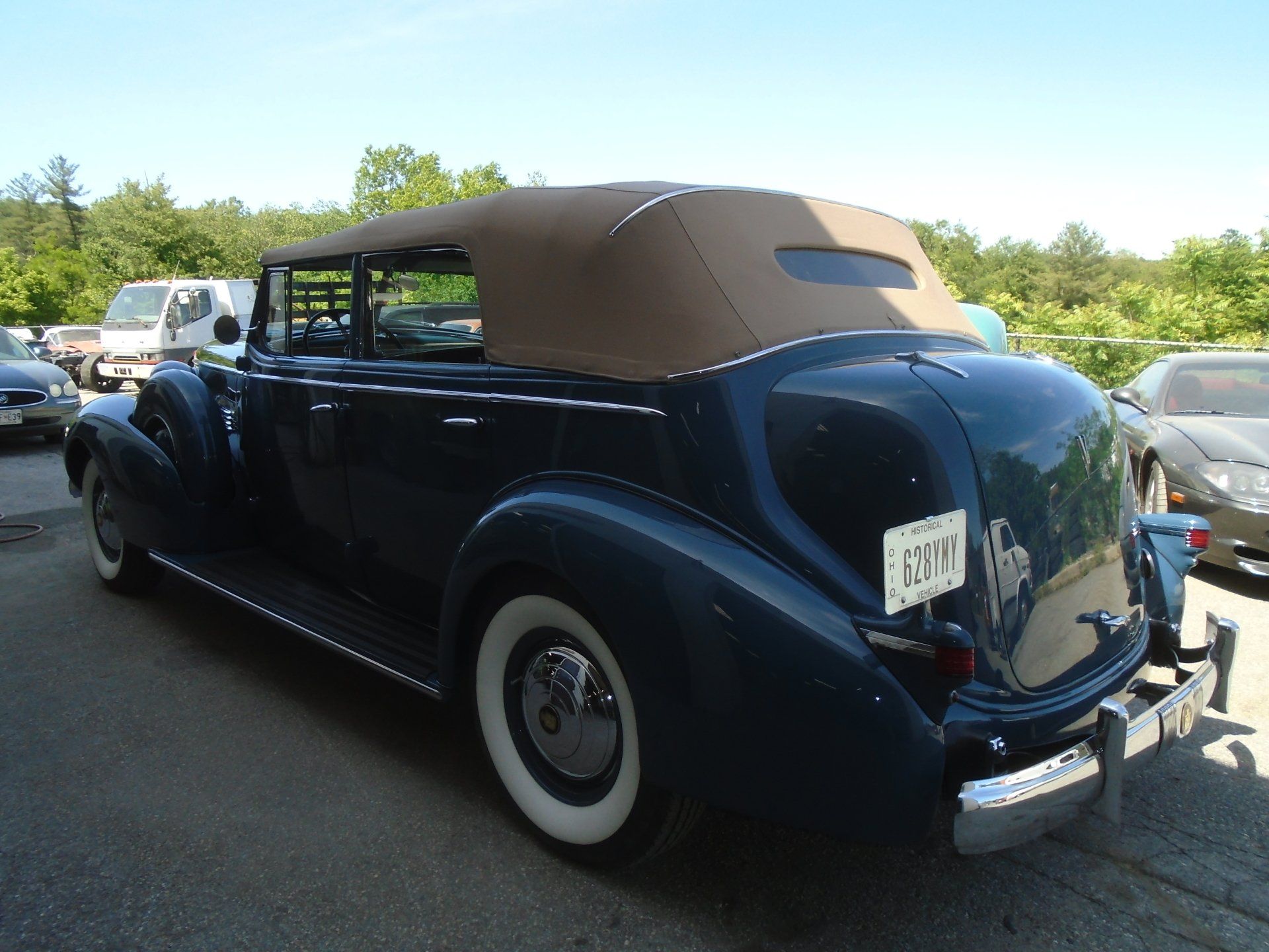 Dark blue classic convertible car with tan top and whitewall tires parked outdoors.