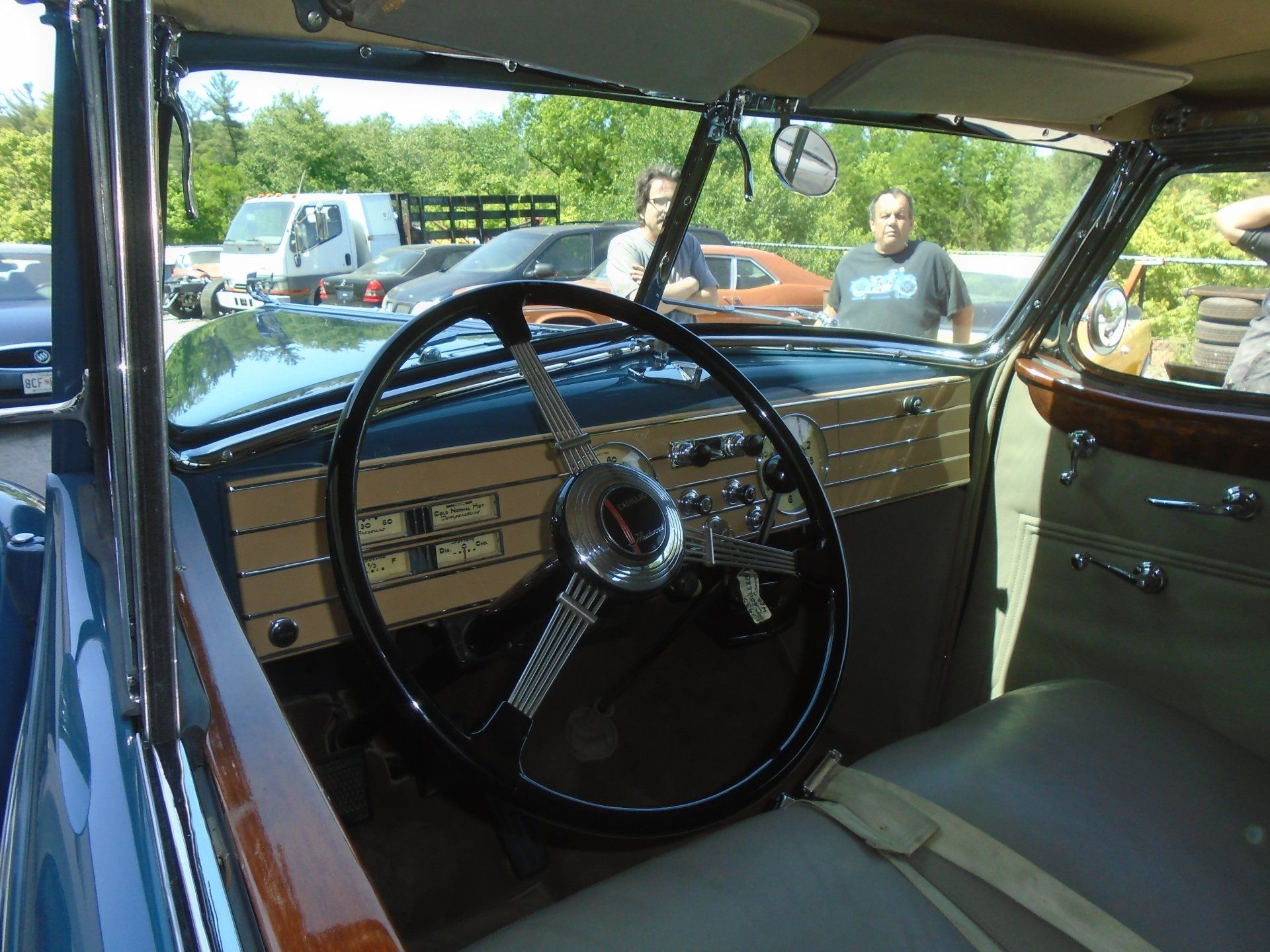 Interior of a classic car with steering wheel and dashboard, two men are standing behind the car looking at the camera.